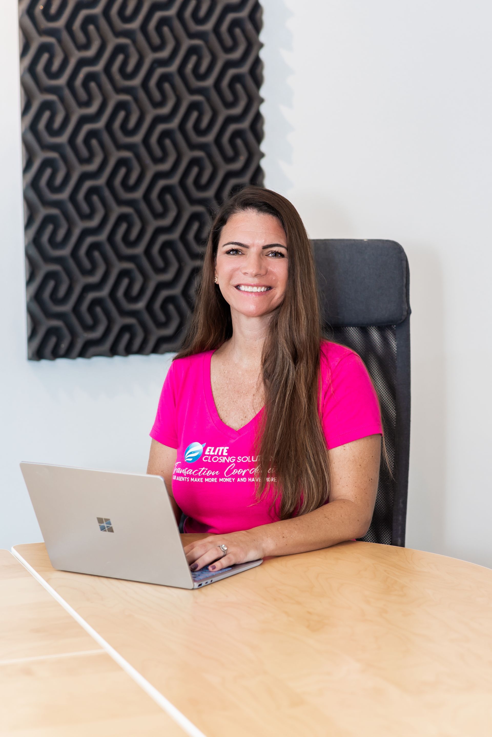 A woman in a pink shirt is sitting at a table with a laptop.