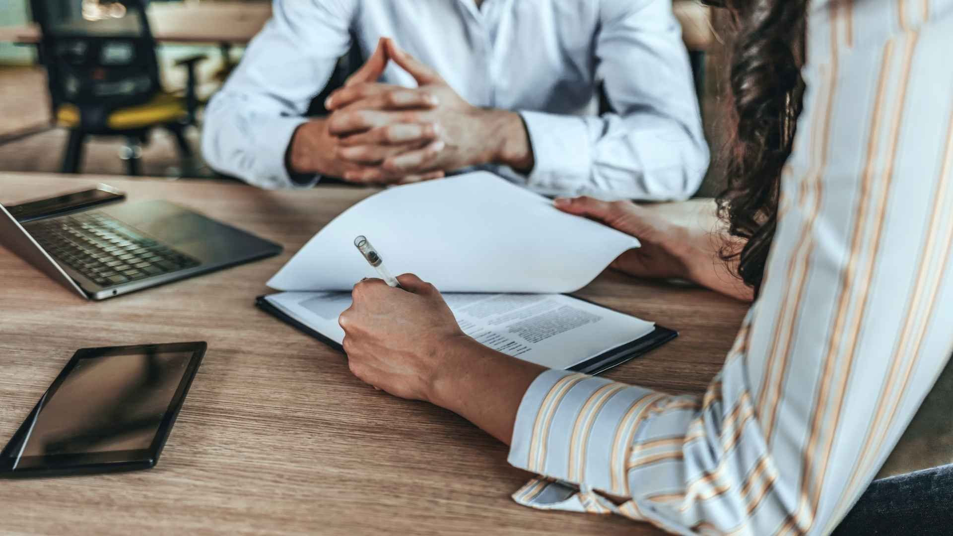 A man and a woman are sitting at a table with papers and a laptop.