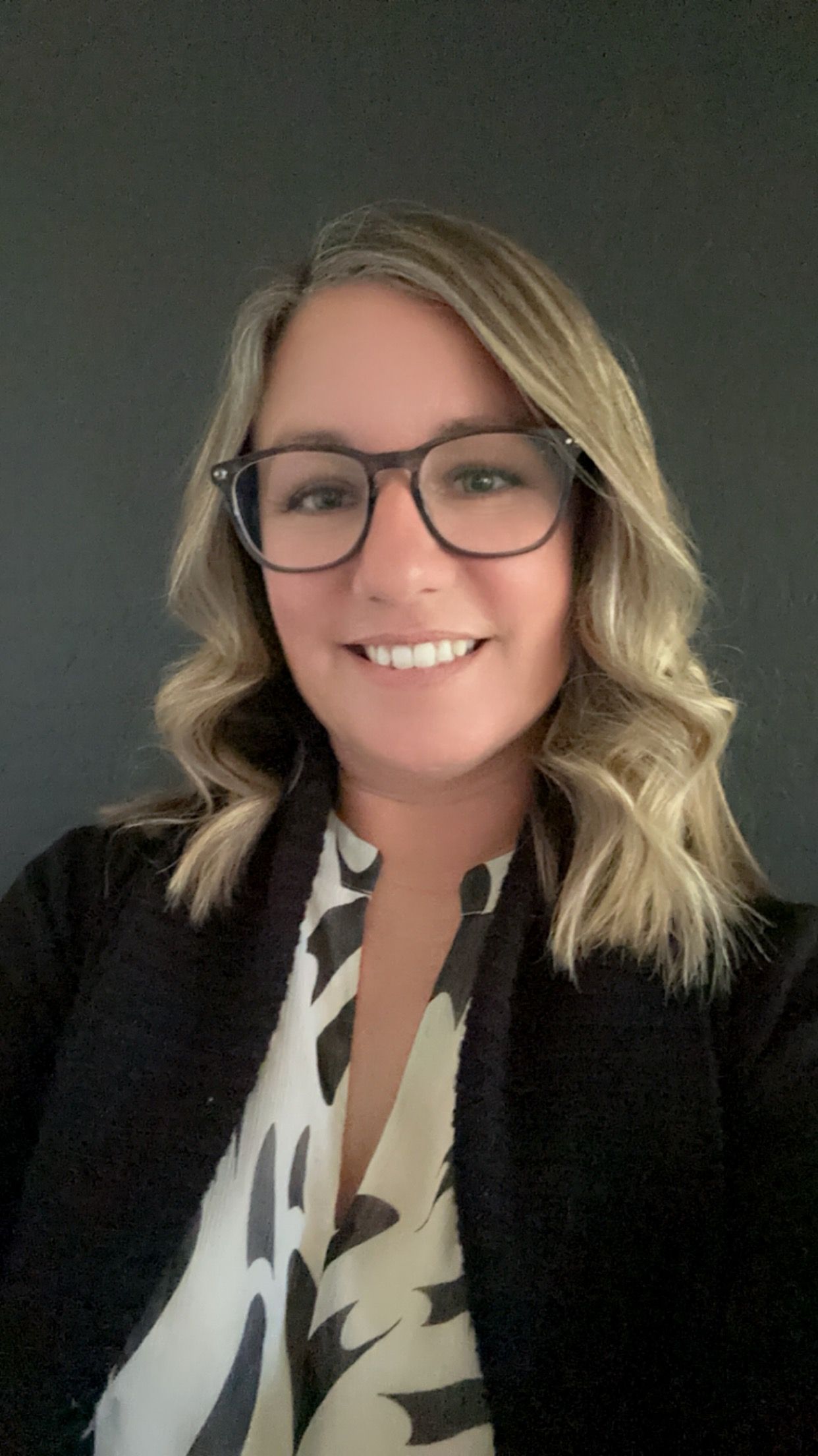 A woman wearing glasses and a black jacket is smiling for the camera.