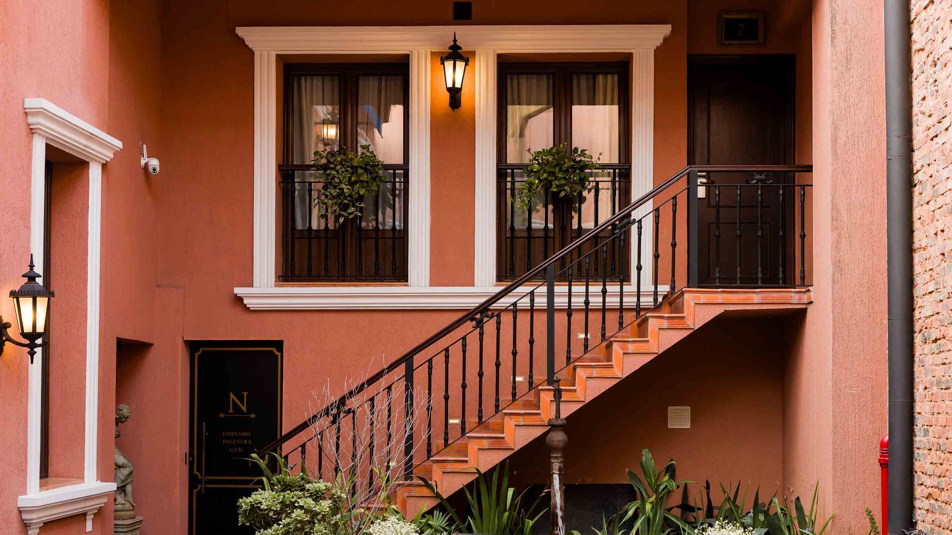 Elegante habitación con mesa de caoba, sofá floral, candelabros antiguos y arte en una pared de ladrillos.