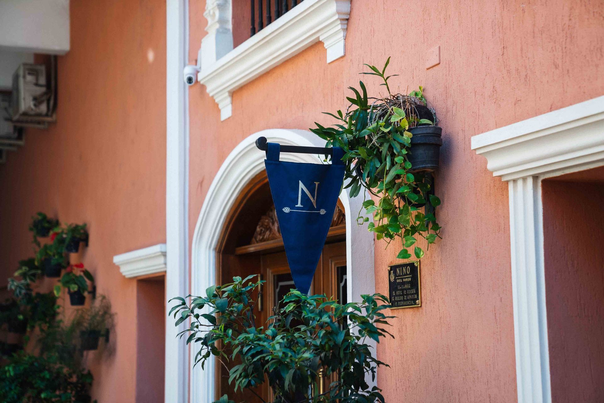 Dos sillones ornamentados flanquean una pequeña mesa con lámpara y obras de arte en una pared gris.