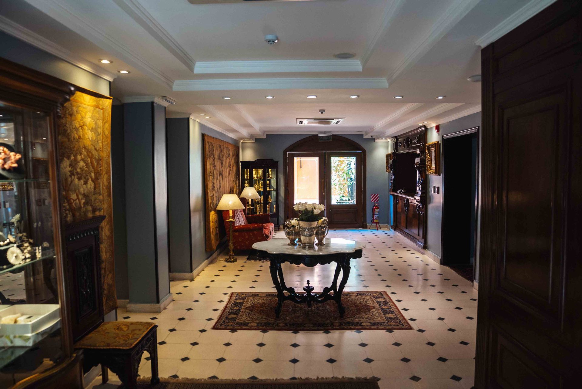 Bandeja de desayuno sobre una cama con sábanas blancas; juego de té de plata, flores, jugo.