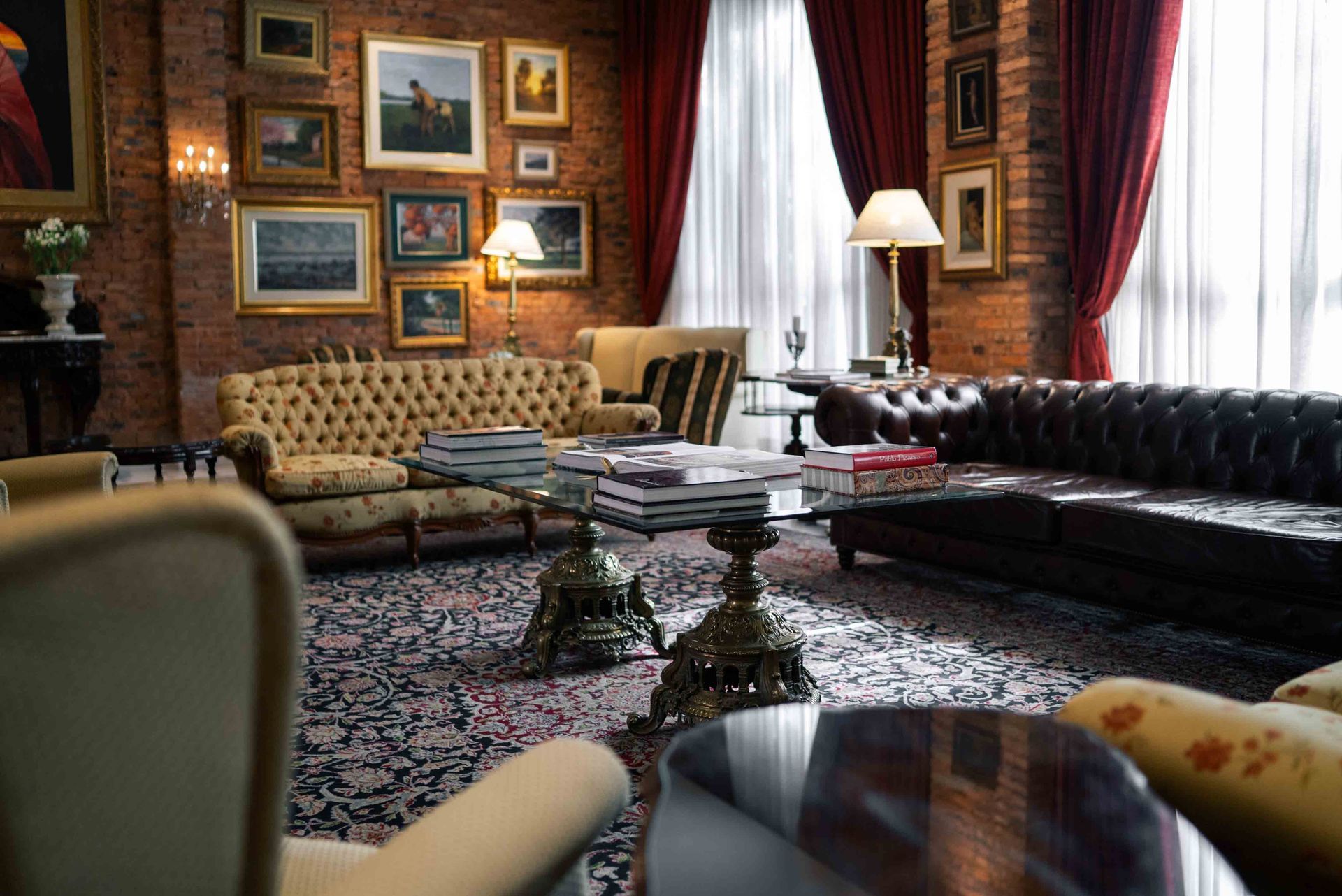 Sala de estar lujosa: jarrón de lirios blancos, candelabros ornamentados, cortinas rojas, piano y alfombras estampadas.