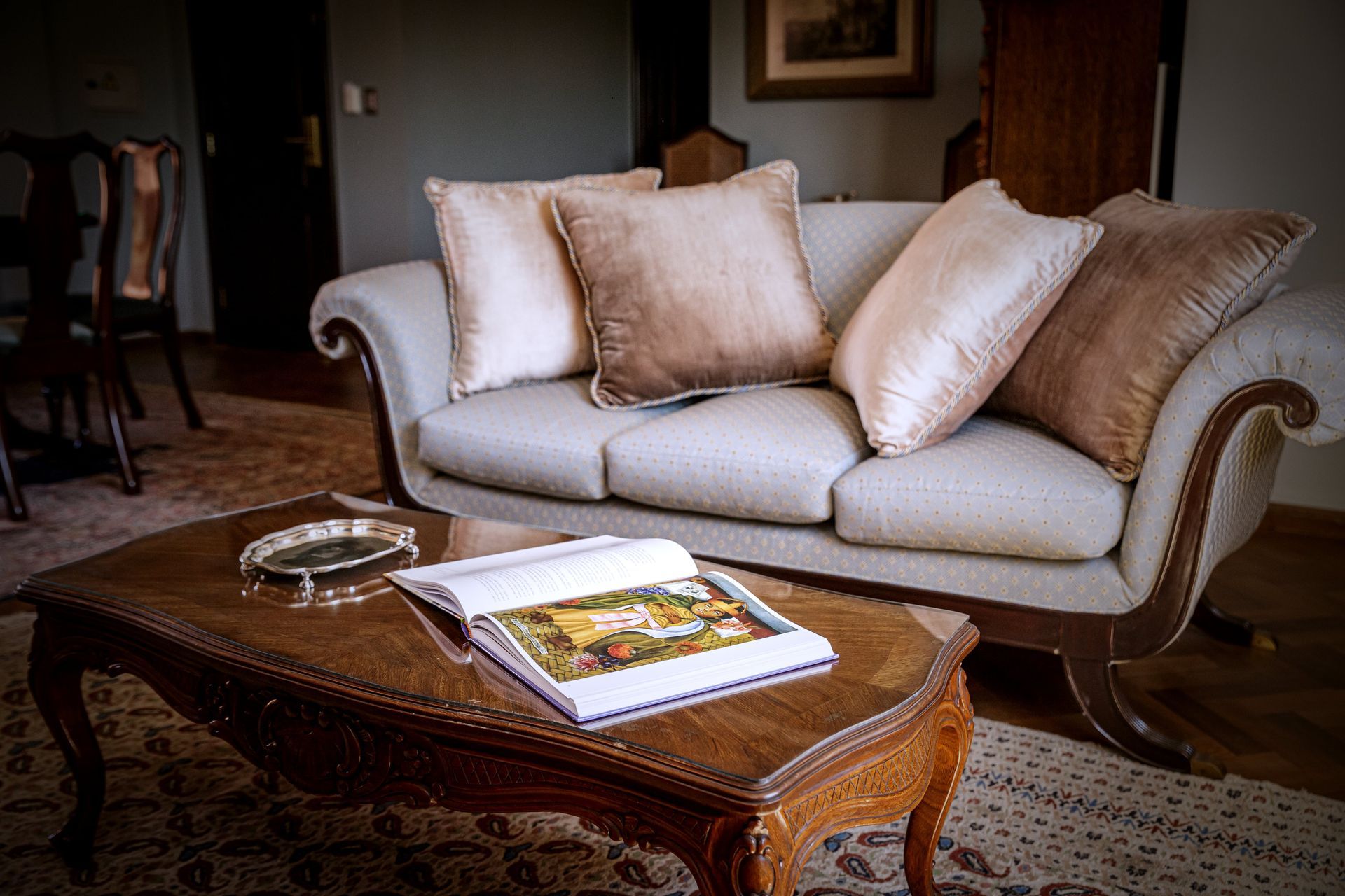 Sala de estar con sofá y mesa de centro. Sofá beige con cojines y un libro sobre una mesa de madera marrón.