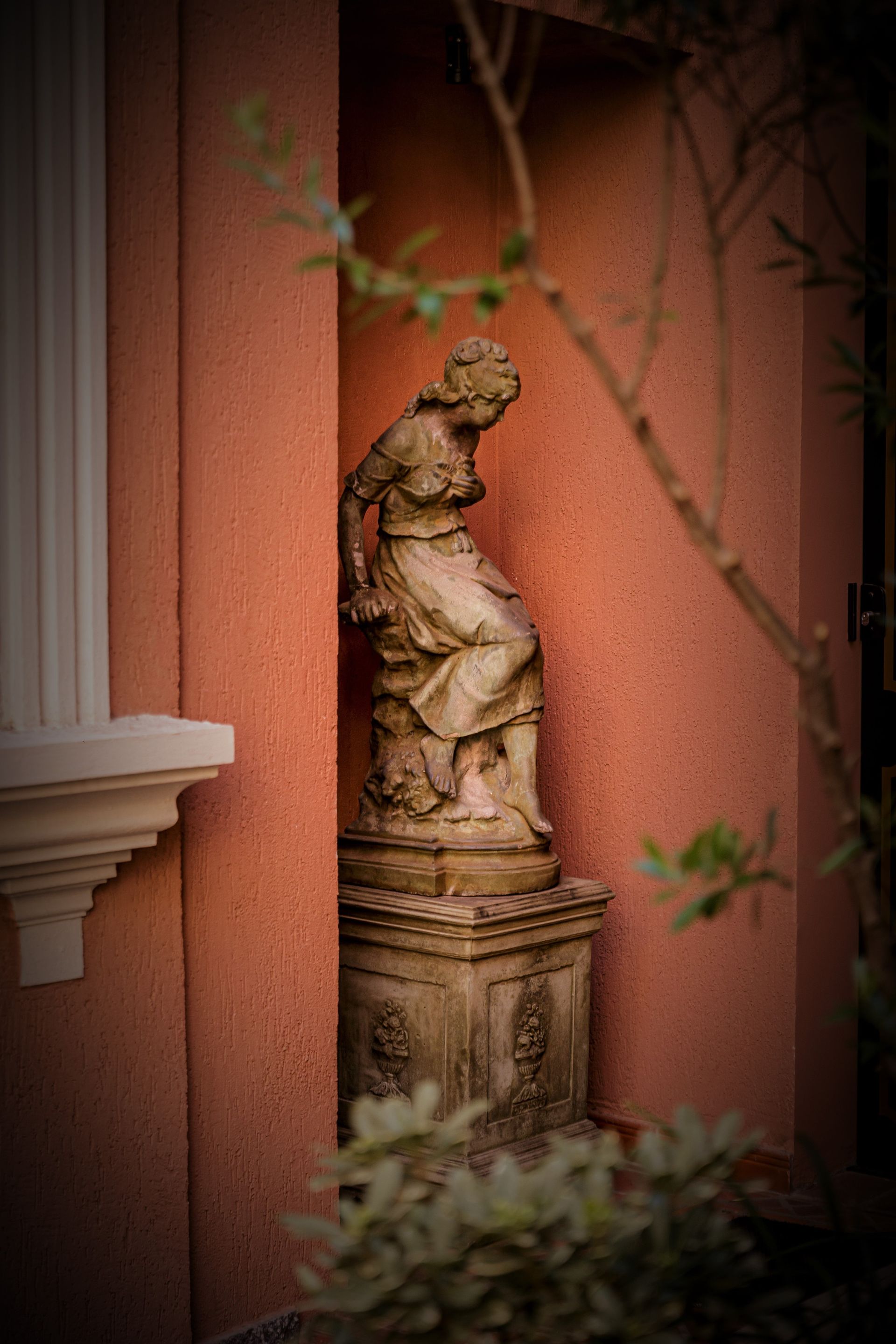 Estatua de mujer sobre pedestal en alcoba de terracota pintada.