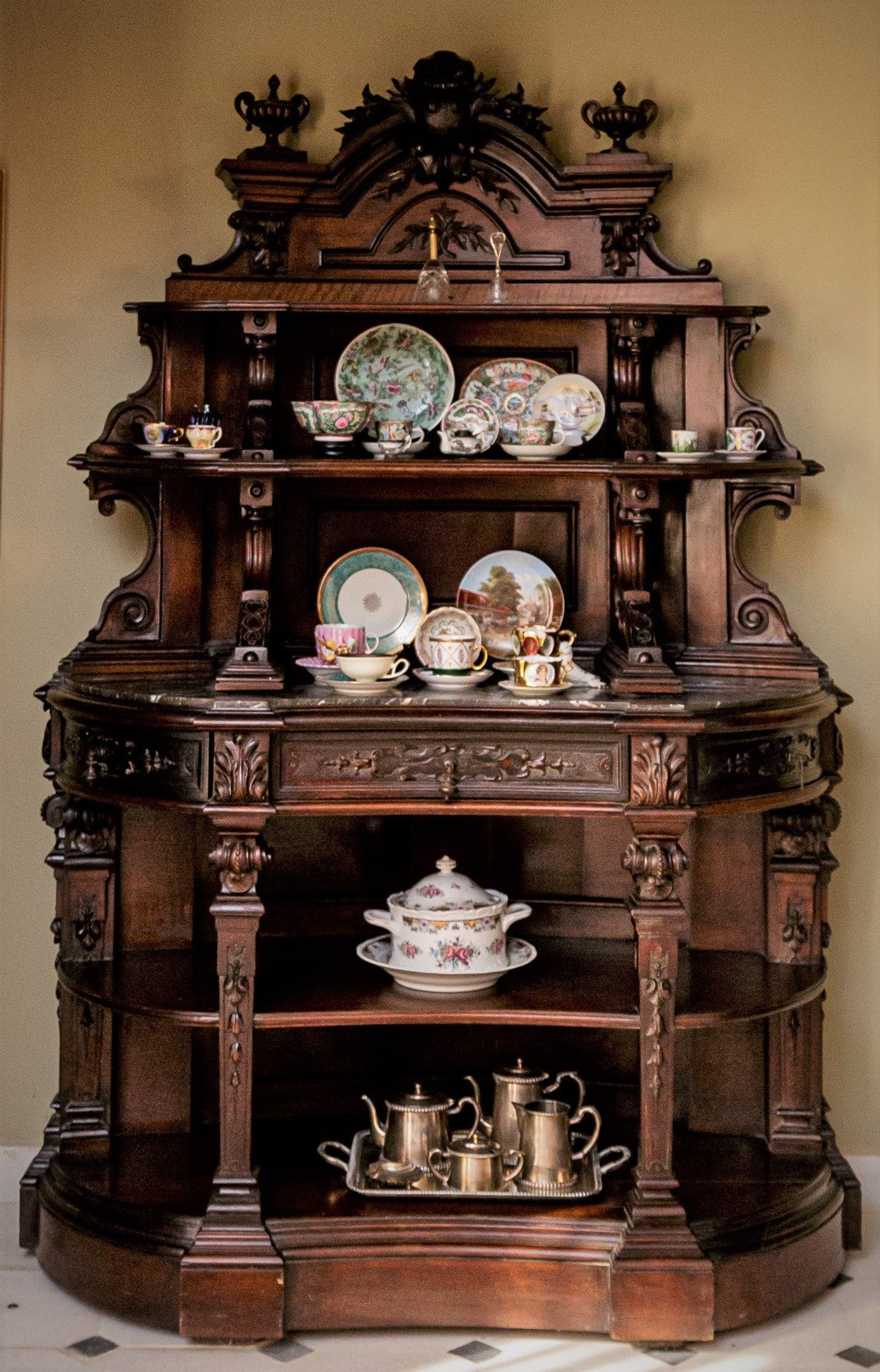 Vitrina de madera ornamentada que exhibe platos antiguos y un juego de té.