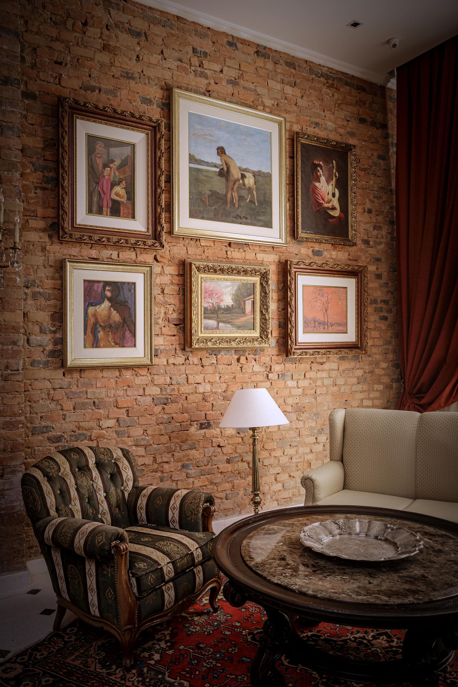 Pared de galería con obras de arte enmarcadas sobre una pared de ladrillos, junto a una silla tapizada.