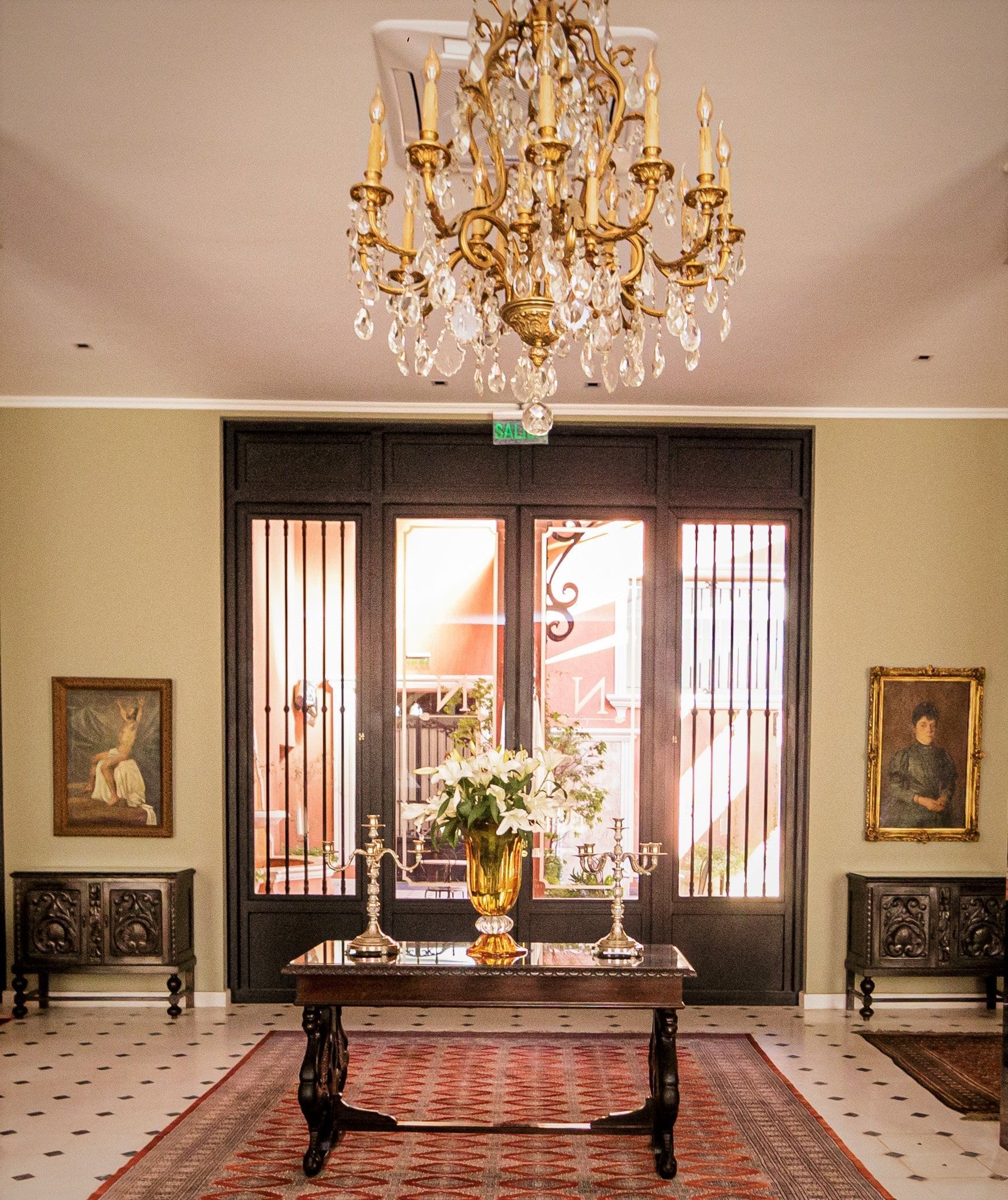 Elegante entrada con lámpara de araña, muebles antiguos y puertas dobles al área exterior.