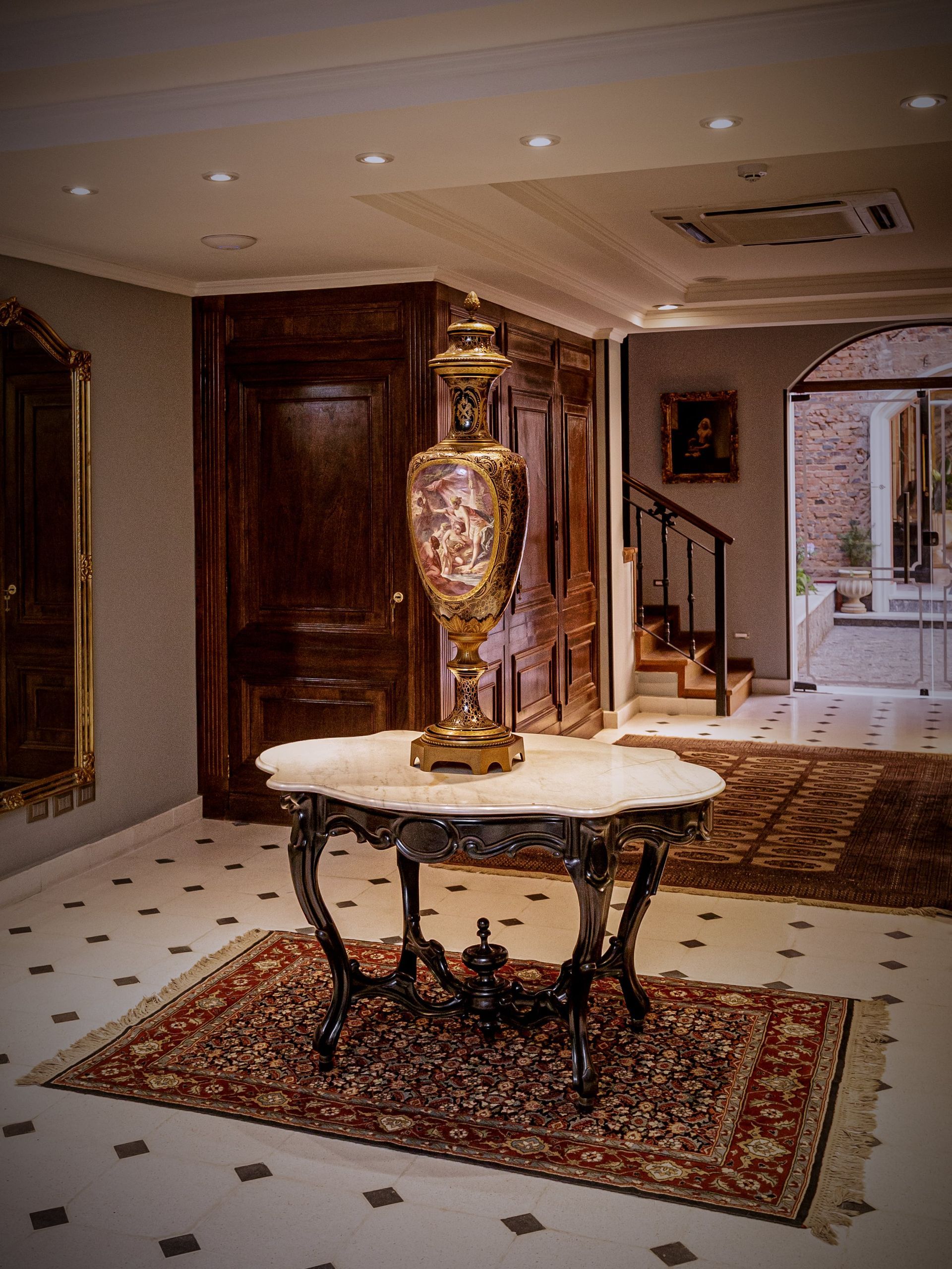 Vestíbulo adornado con jarrón decorativo sobre una mesa con cubierta de mármol, alfombra oriental.