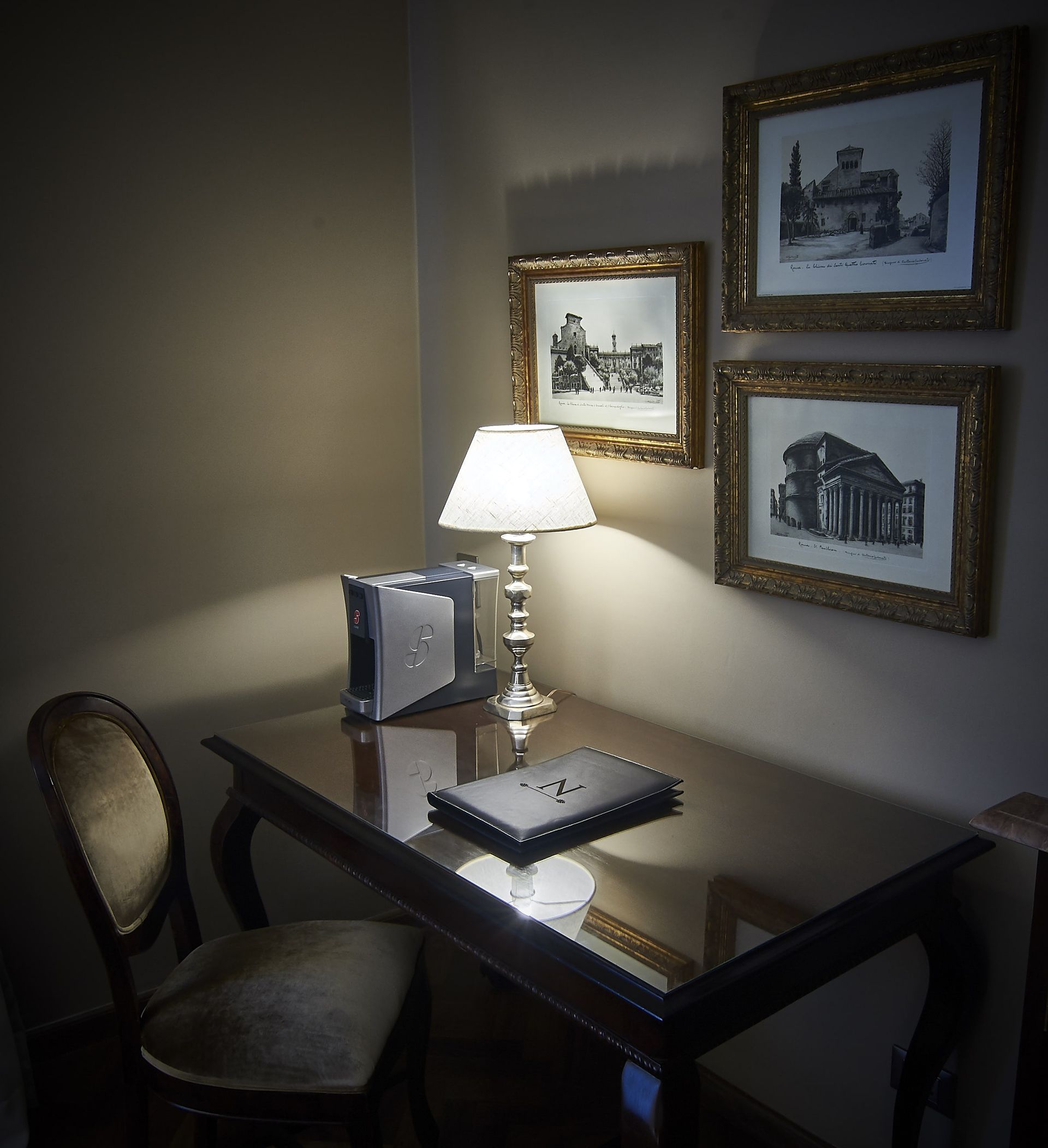 Escritorio con lámpara, silla y arte enmarcado en un rincón de una habitación, iluminado por una luz cálida.