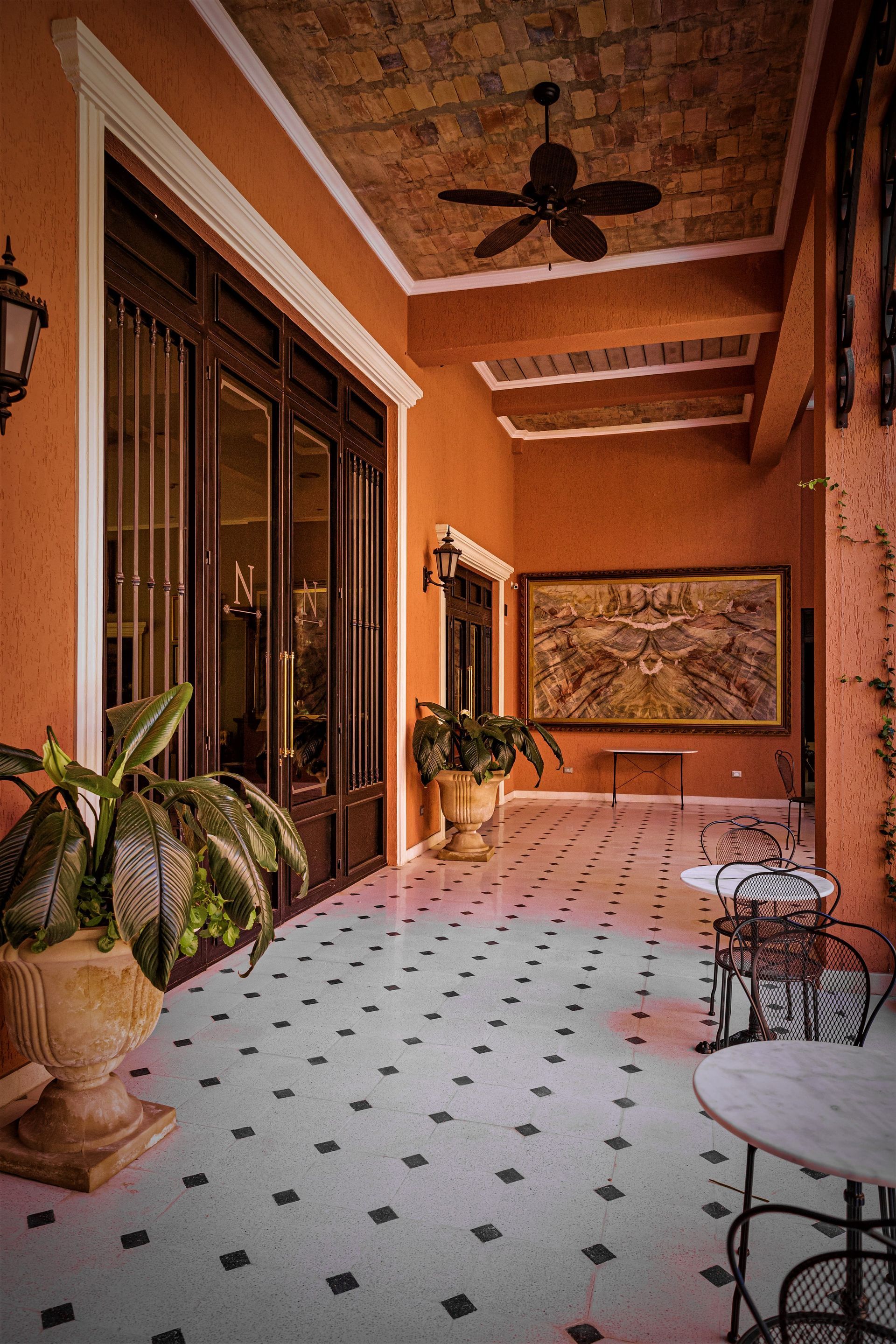 Terraza con paredes naranjas, suelo de baldosas blancas y negras, puertas de madera oscura y decoración ornamentada.