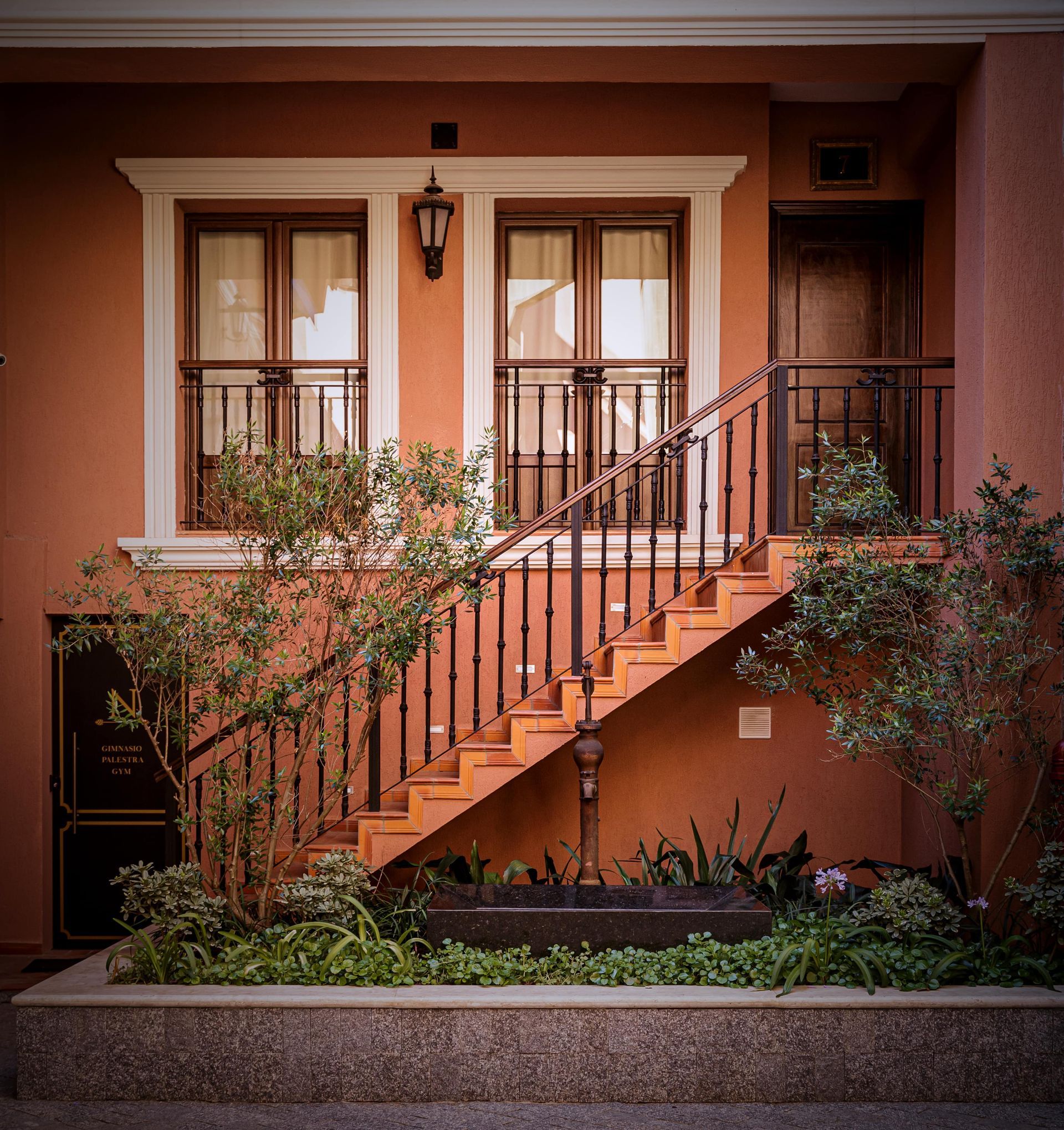 Exterior del edificio con escaleras que conducen a un portal, flanqueado por ventanas y con una baranda de hierro forjado.