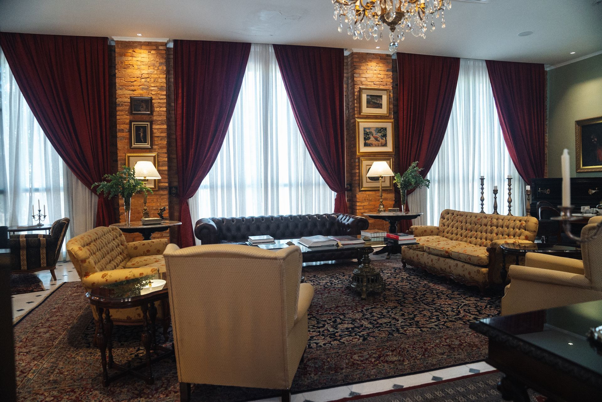 Un lujoso salón con cortinas de color rojo oscuro, sofás capitoné y una decoración ornamentada sobre paredes de ladrillo y una alfombra estampada.