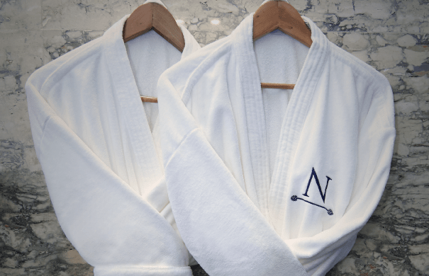 Dos batas blancas colgadas en perchas de madera, una de ellas con una 