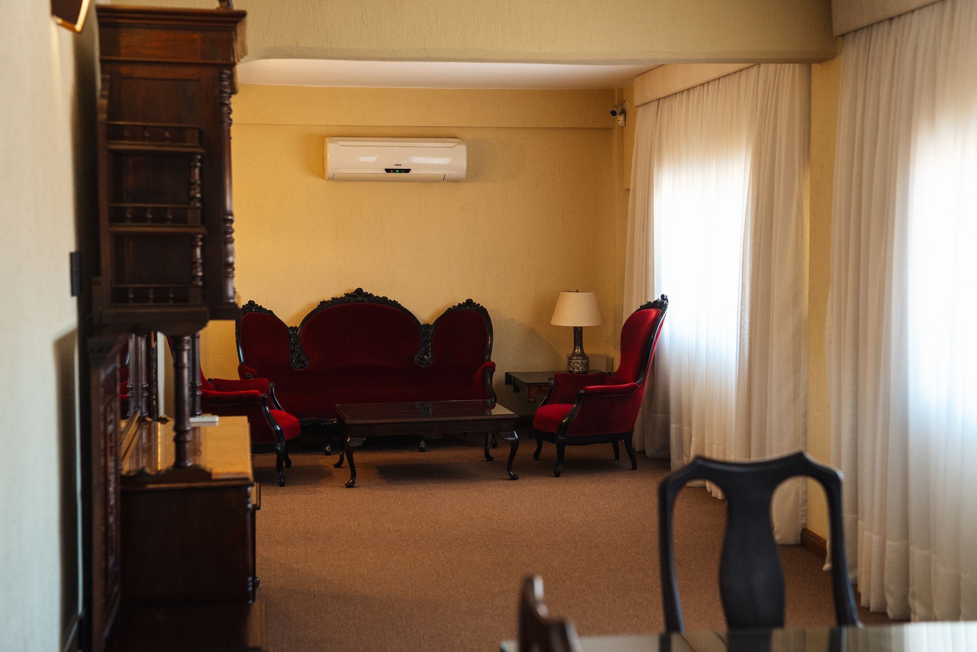 Una sala de estar con muebles rojos de estilo vintage, que incluyen un sofá y sillones, situada sobre un suelo alfombrado y con aire acondicionado.