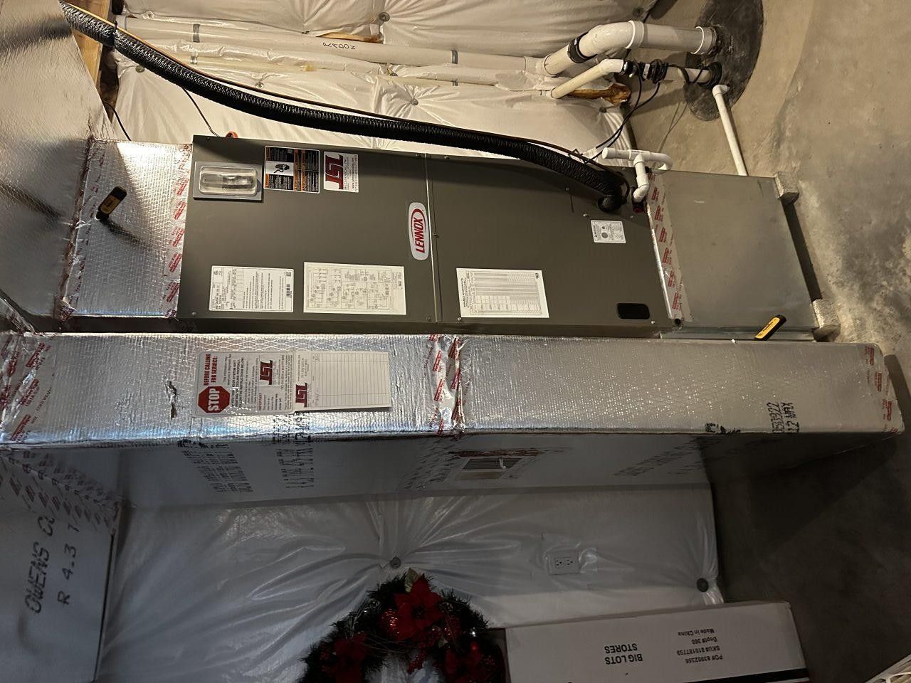 An HVAC air handler and ductwork system mounted horizontally in a basement with white insulated walls.