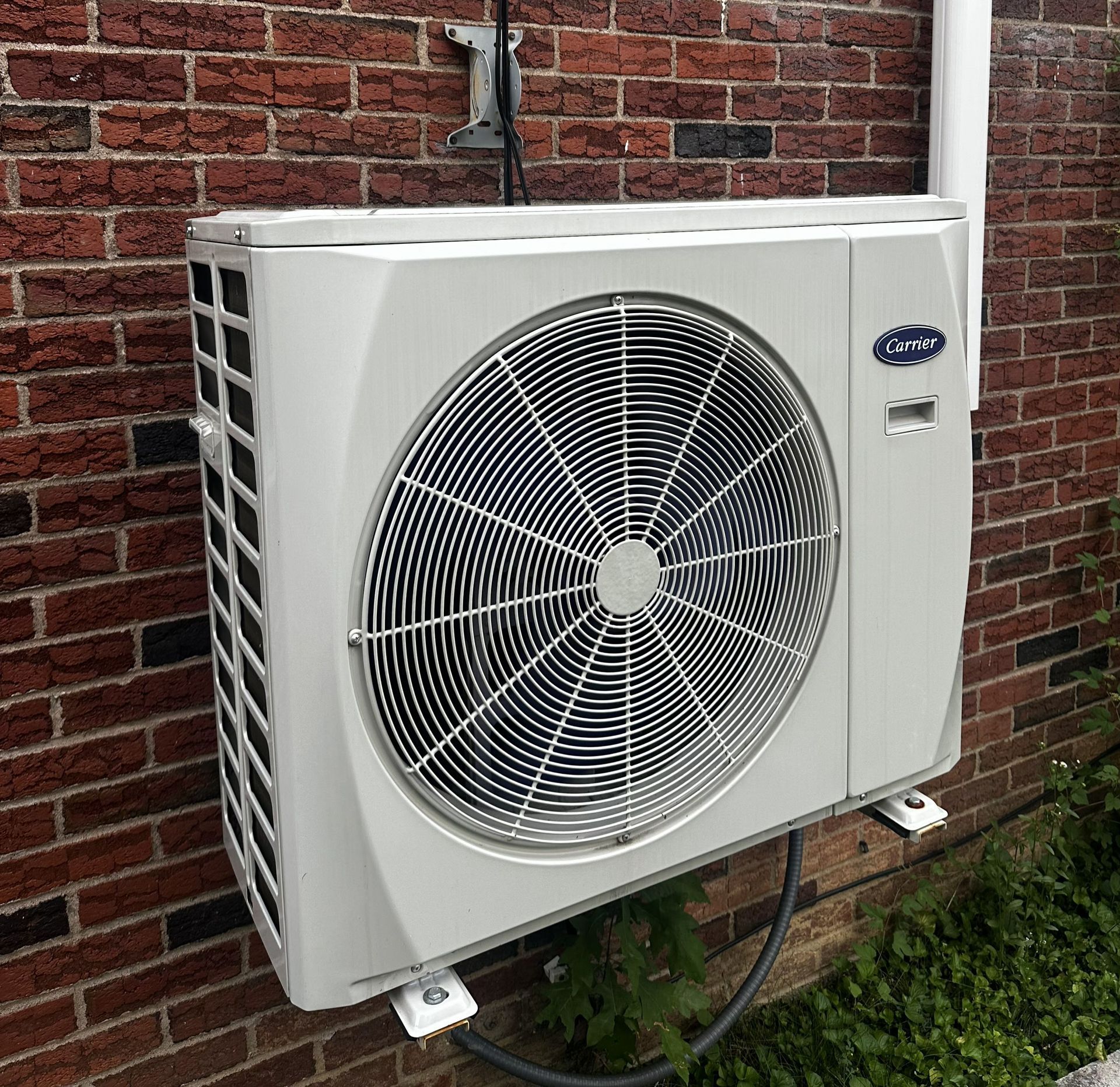 A white HVAC outdoor unit mounted on a brick wall.
