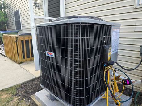 An outdoor HVAC condenser unit on a concrete pad next to a house, with yellow diagnostic gauges attached to the side.
