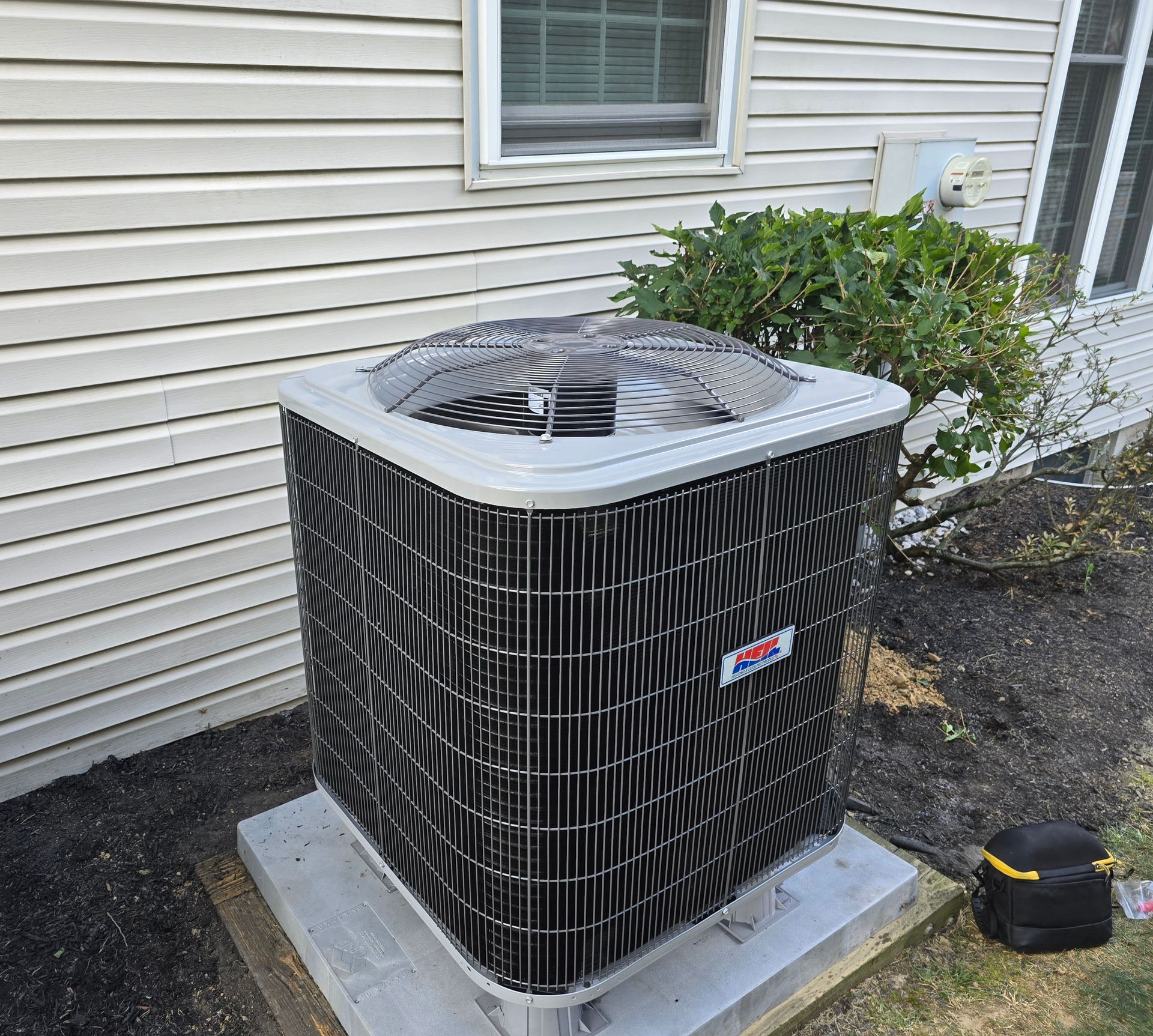 A gray outdoor central air conditioning unit sits on a concrete pad next to a beige-sided house.
