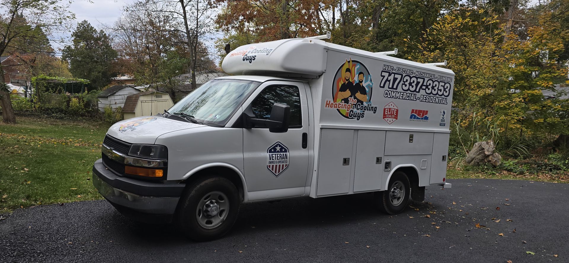 White Chevy work truck with custom graphics parked on a gravel driveway near trees.