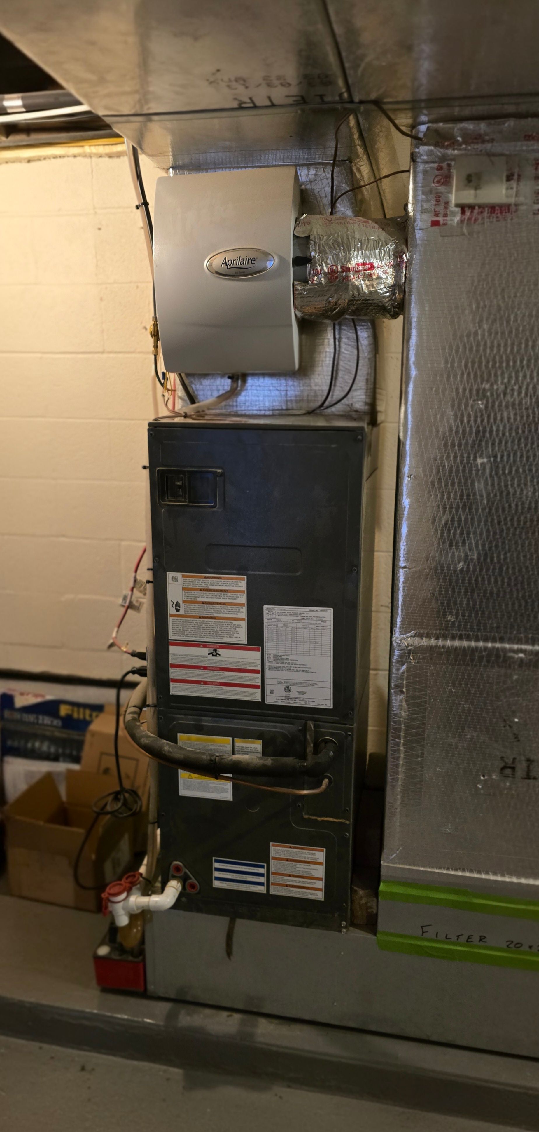 A gray furnace unit with a silver electronic air cleaner mounted above it, installed in a basement.