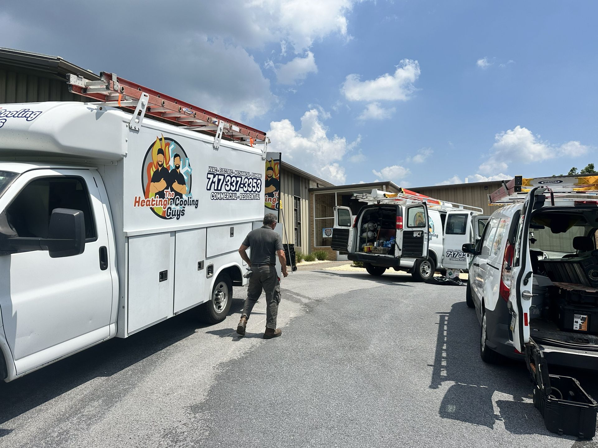 Three work vans parked in a gravel lot on a sunny day with a technician walking toward the building.