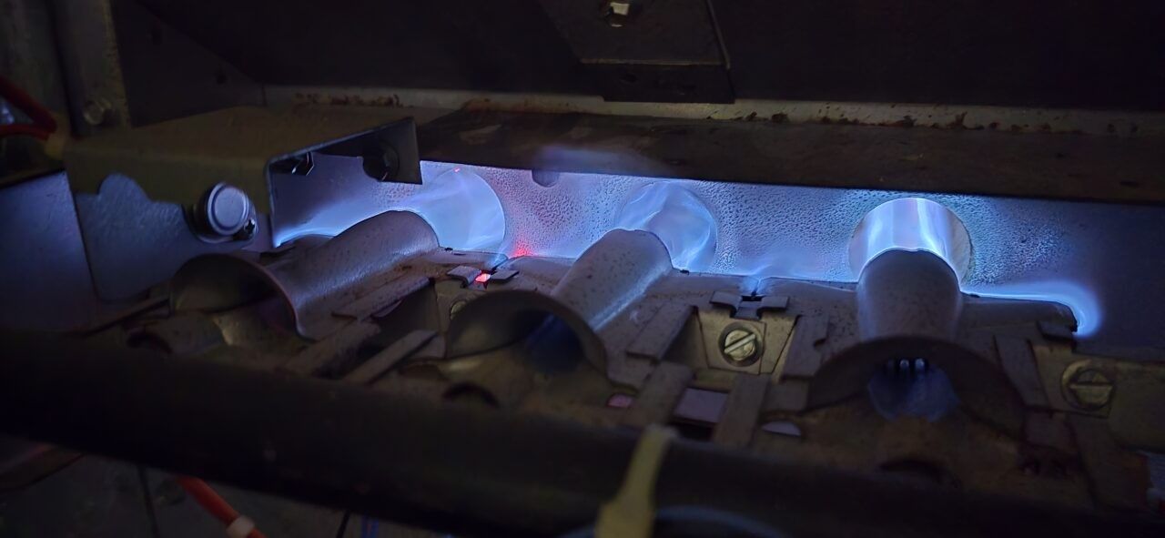 Close-up of a gas furnace interior with bright blue flames burning through metal burners.