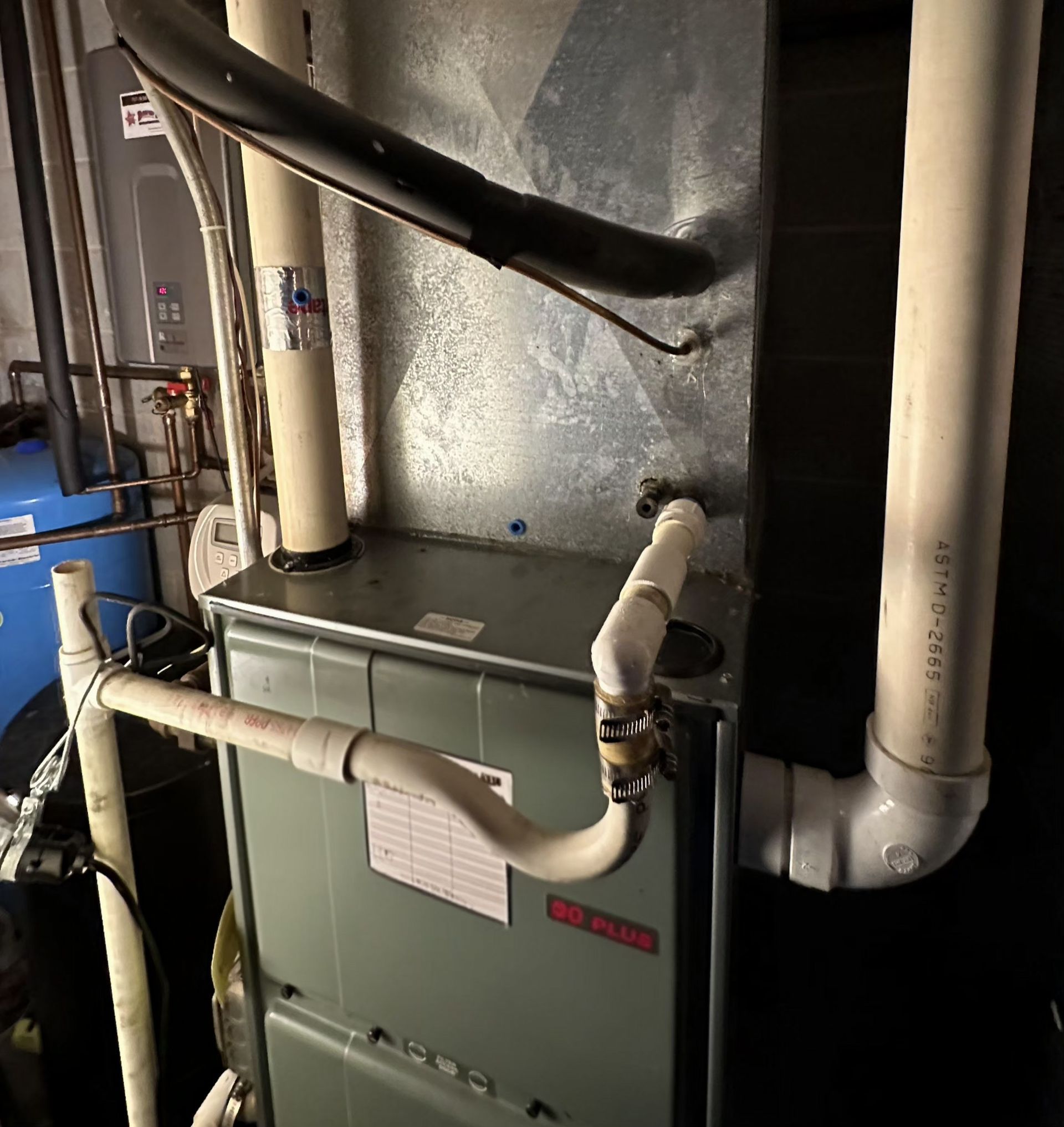 A high-efficiency furnace with white PVC exhaust and condensate drain pipes in a mechanical room.