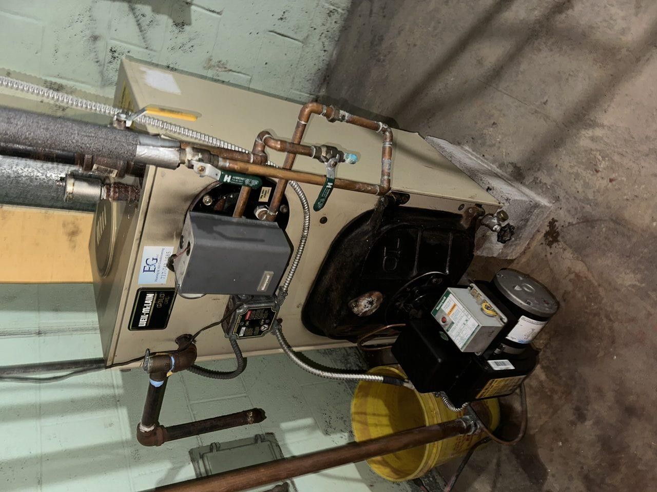 A residential oil-fired boiler in a basement, featuring copper piping and an attached electrical burner motor.