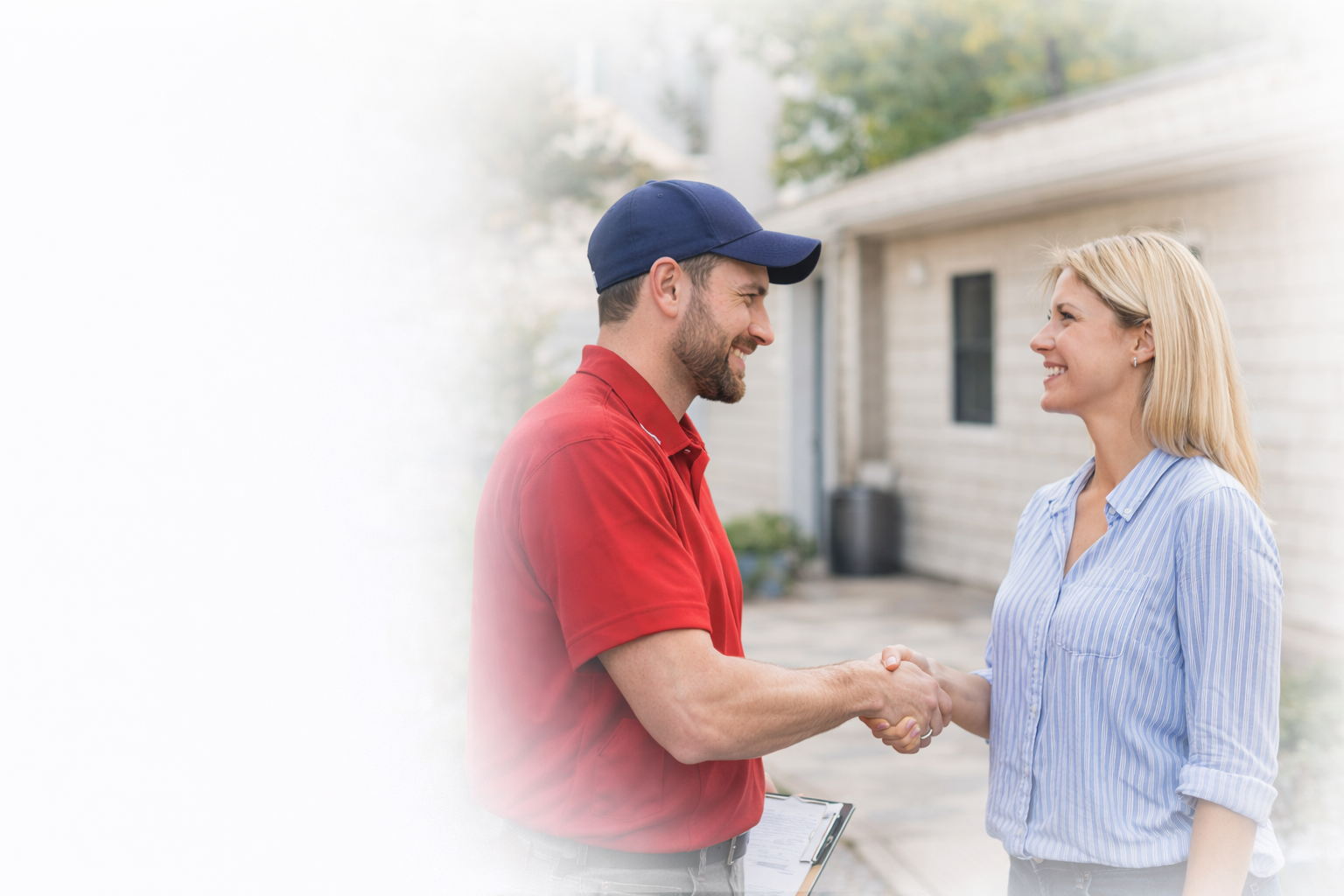 A service professional in a red shirt and blue cap shakes hands with a person in a blue striped shirt outside a home.