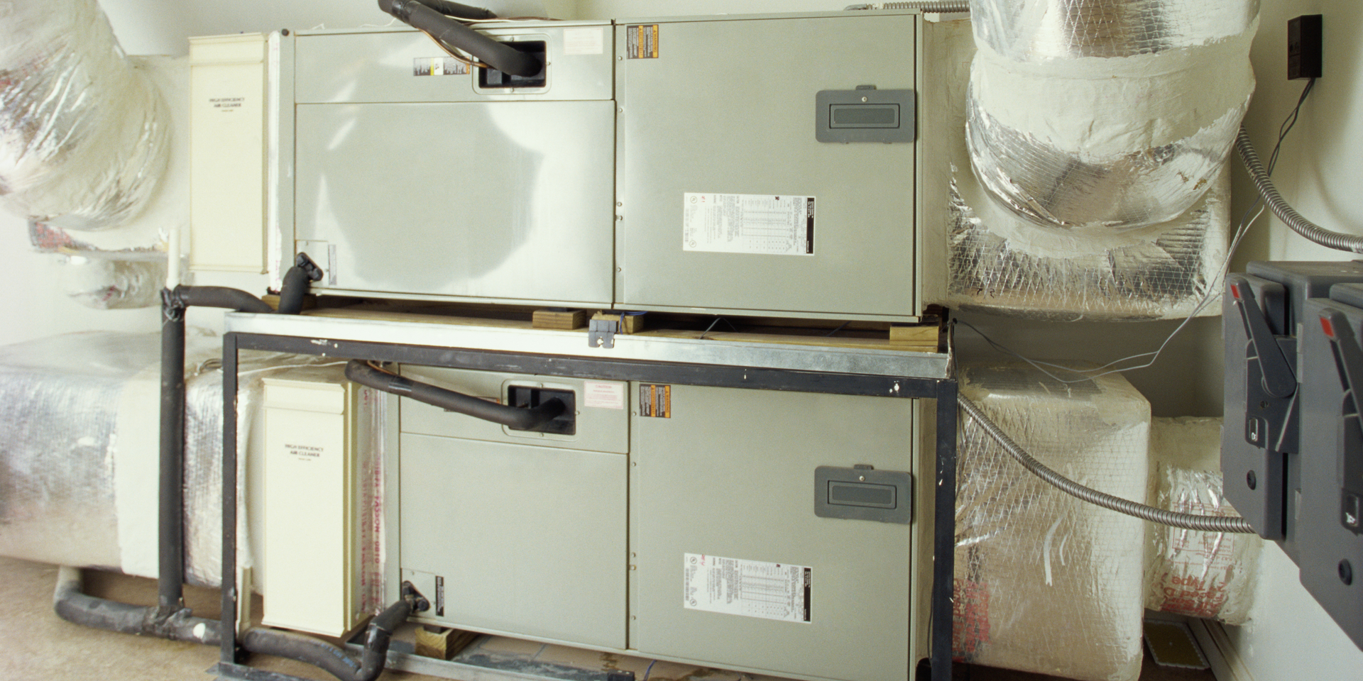 Two stacked horizontal HVAC furnace units installed on a metal frame with connected metal and insulated ductwork.