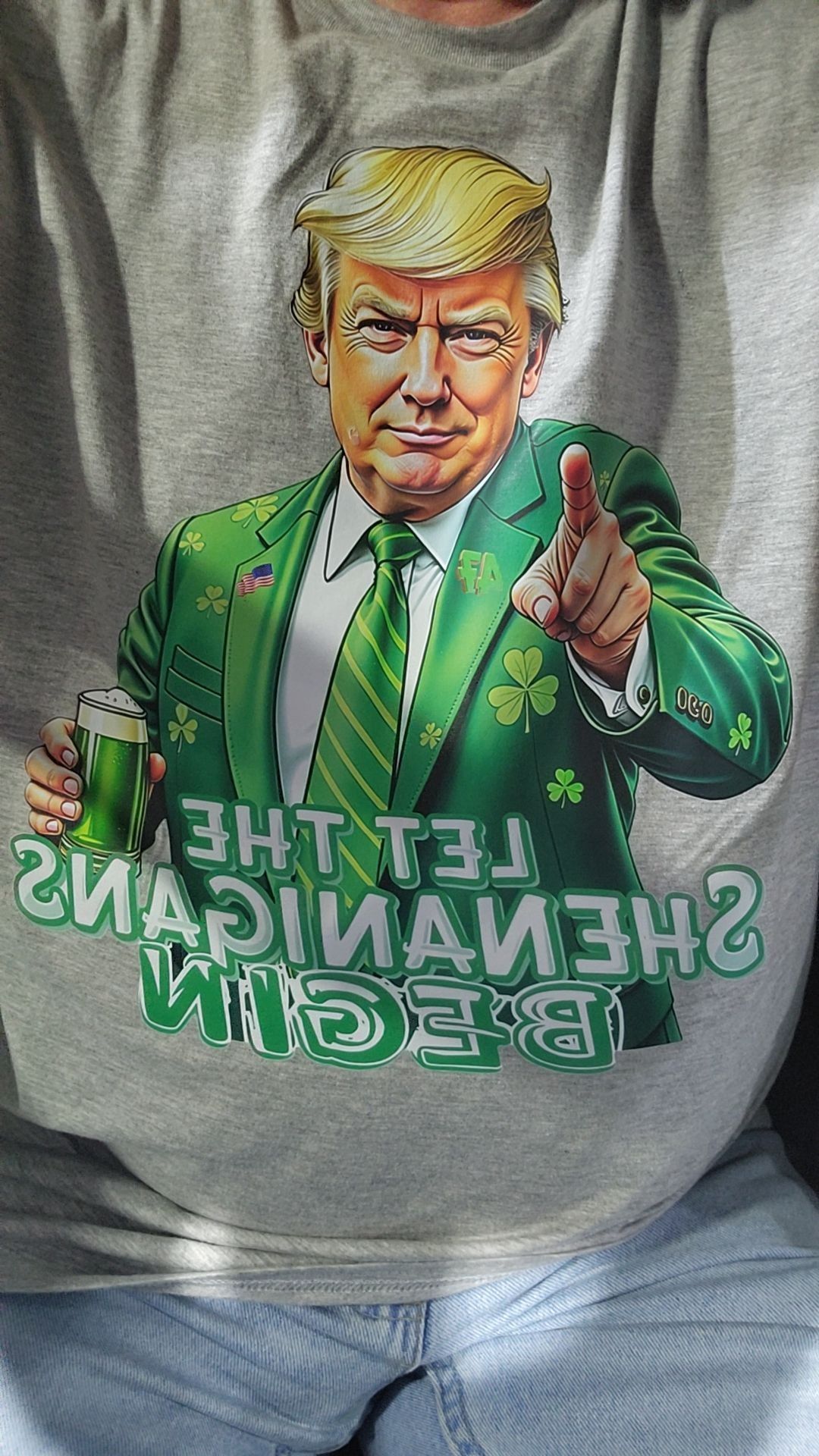 Donald Trump wearing a green suit with shamrocks, pointing, holding a beer, shirt says 