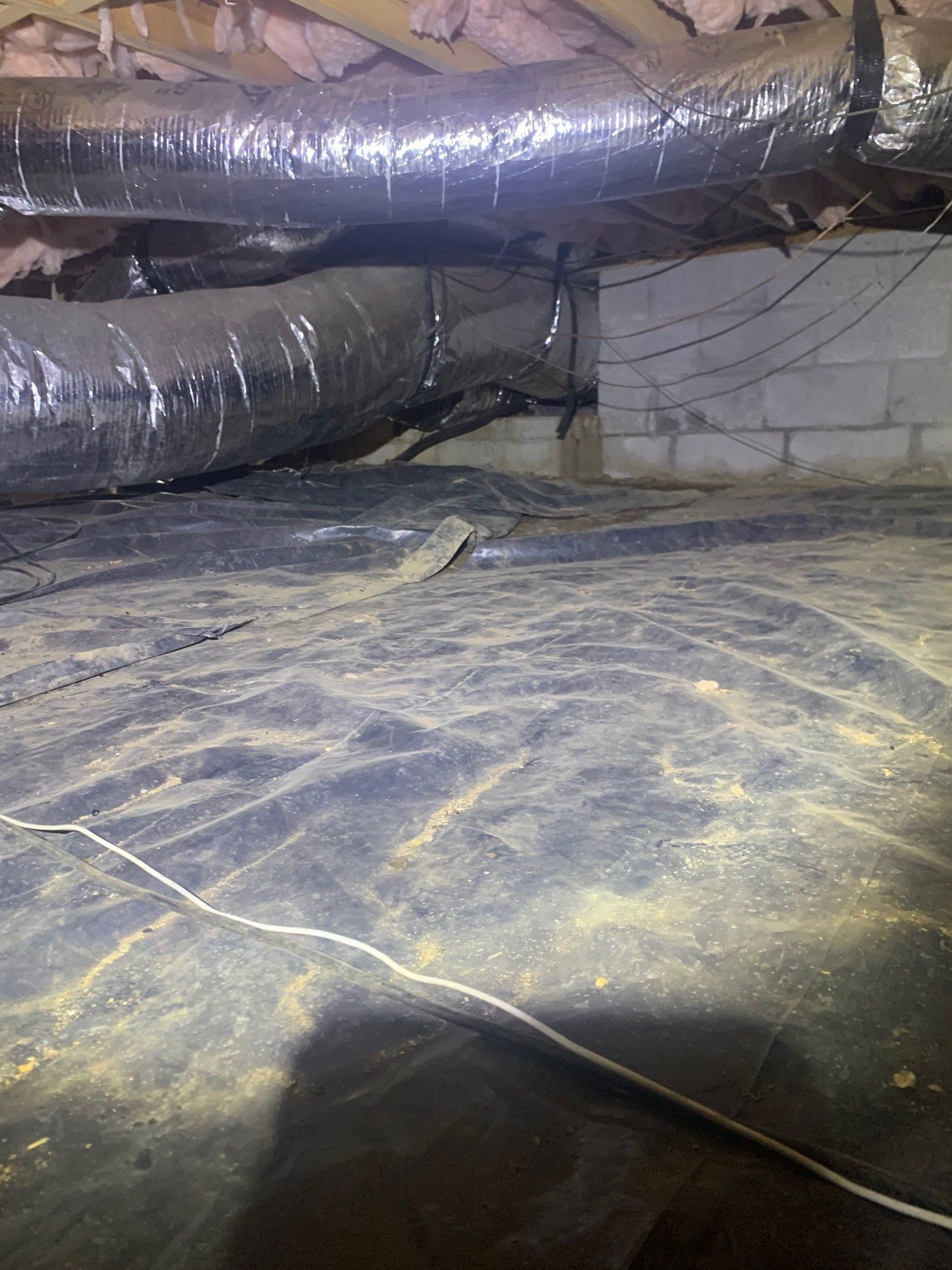 A dirty basement with a lot of pipes and ducts.