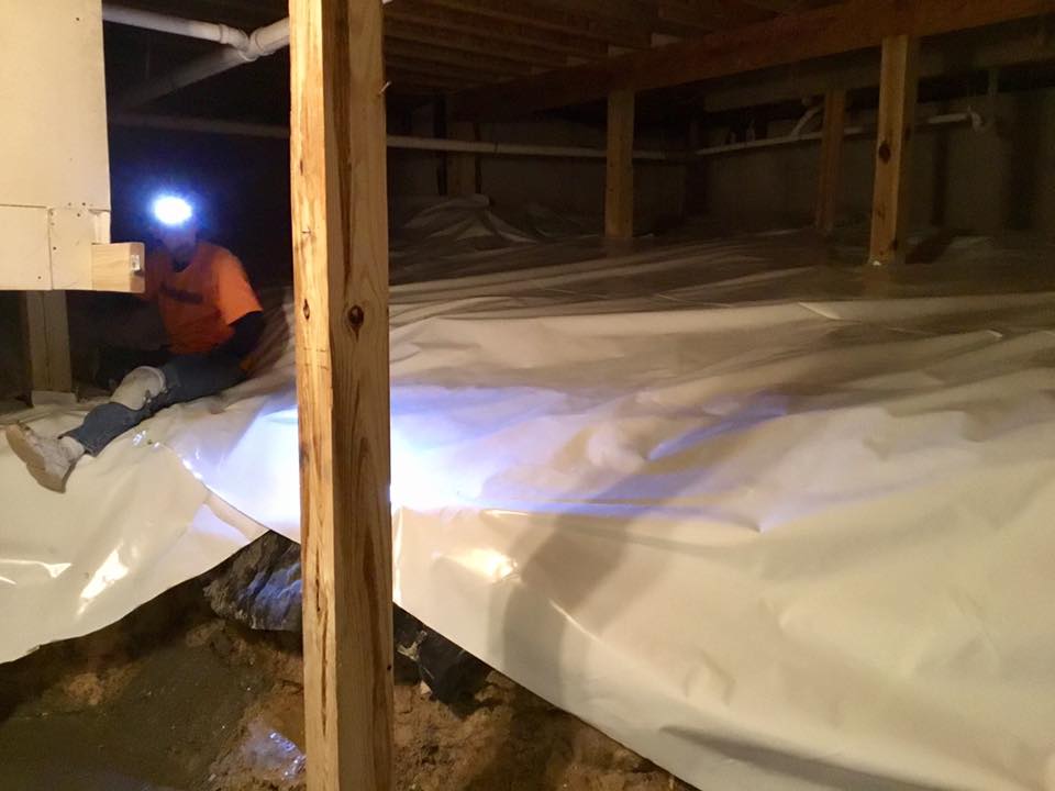 A man is laying on a sheet of plastic in a basement.
