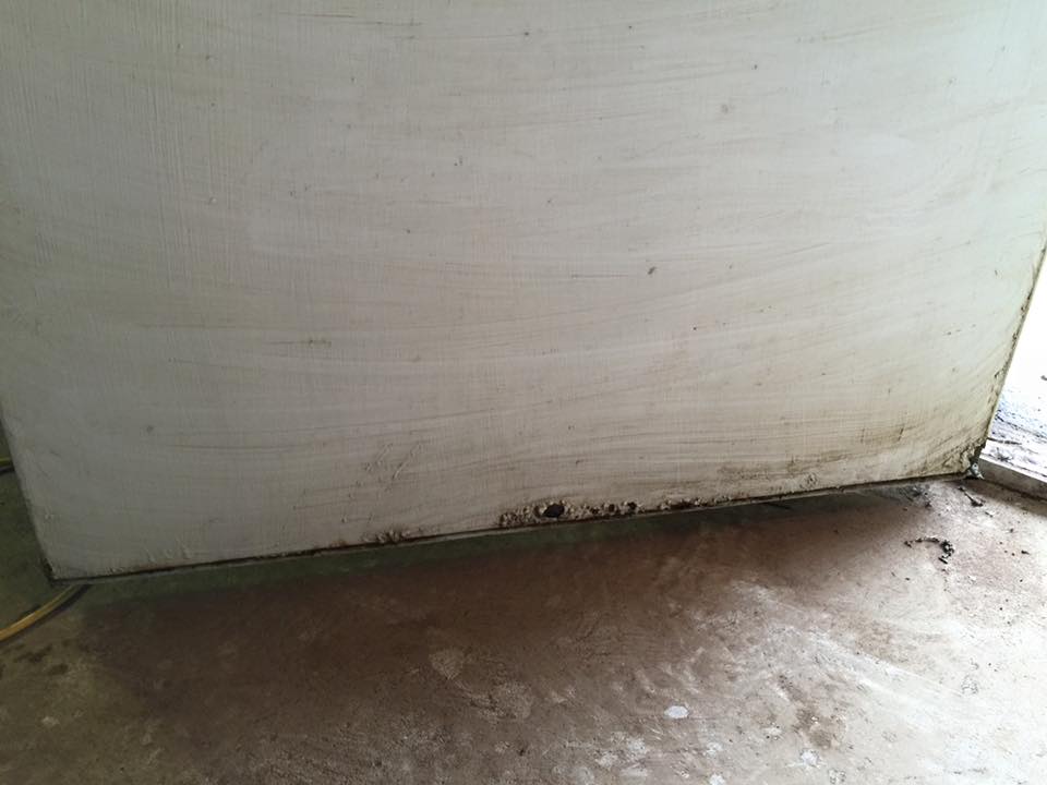 A white box is sitting on a dirty floor next to a door.