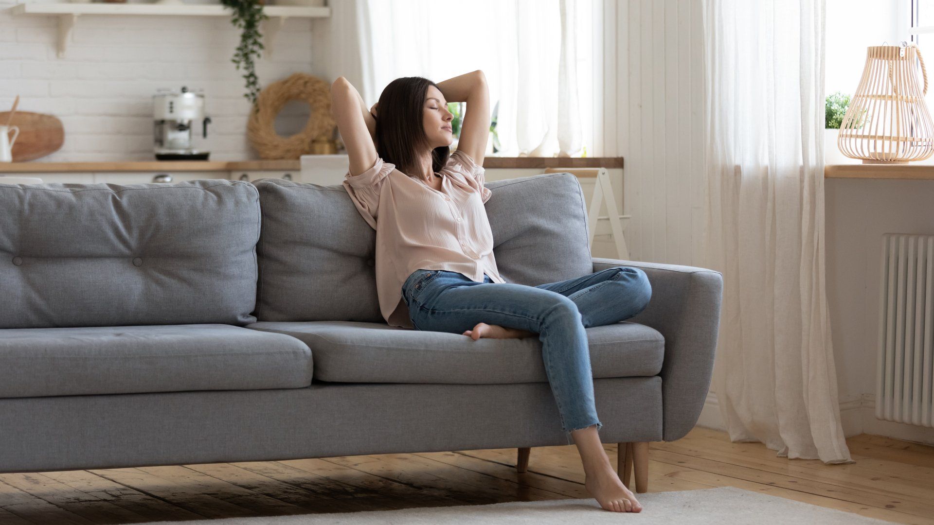 A woman is sitting on a couch in a living room with her arms outstretched.