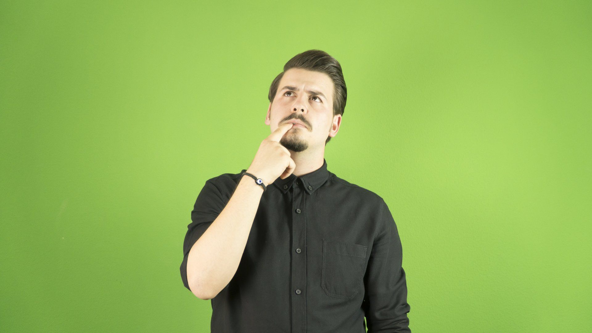 Young man with black shirt thinking for an idea, his finger on his mouth.
