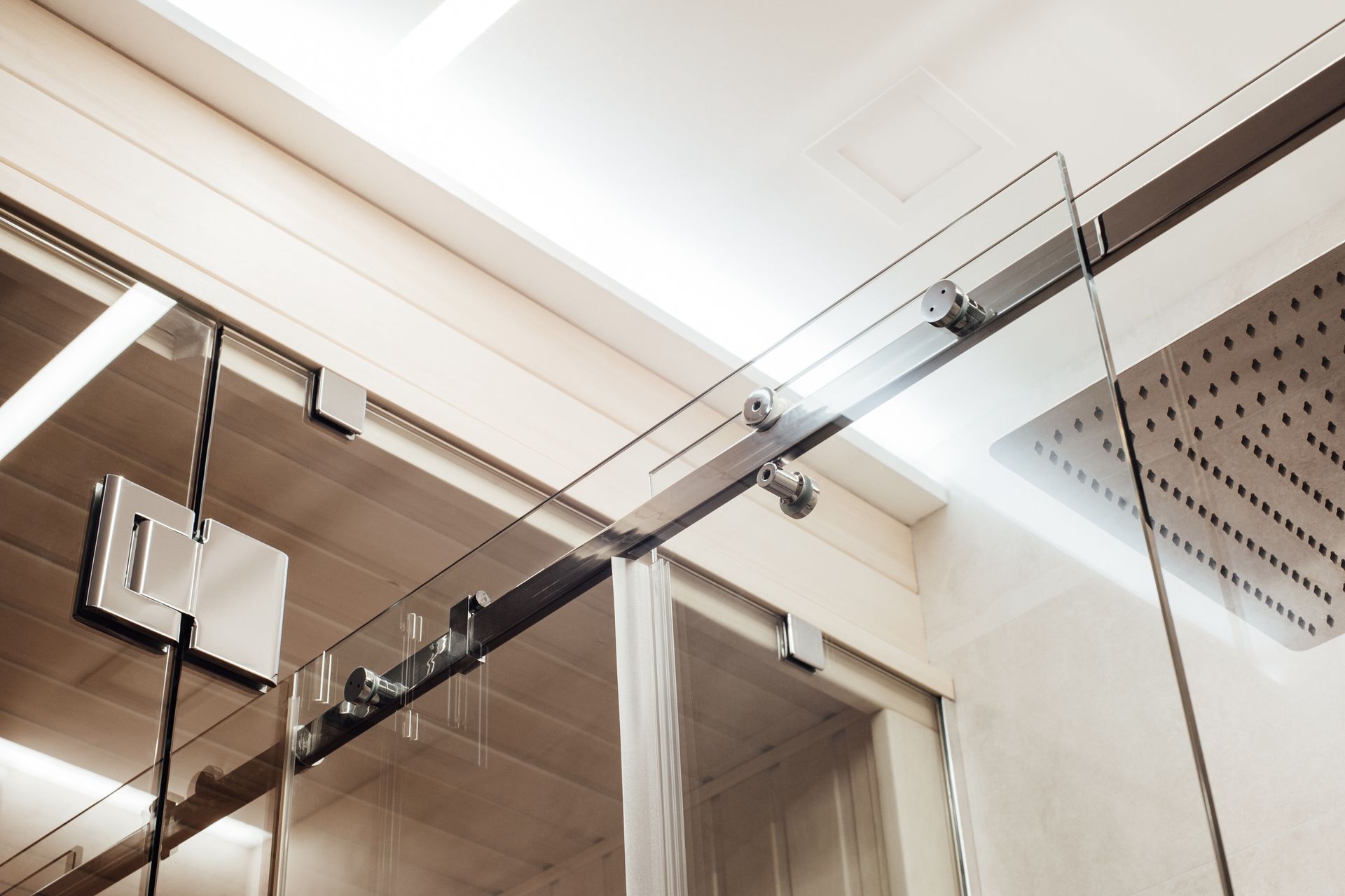 Glass shower door with metal sliding rail and hinge in modern bathroom interior.
