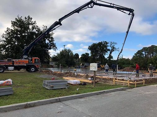 A construction site with a large crane pumping concrete into a foundation area while workers stand nearby.