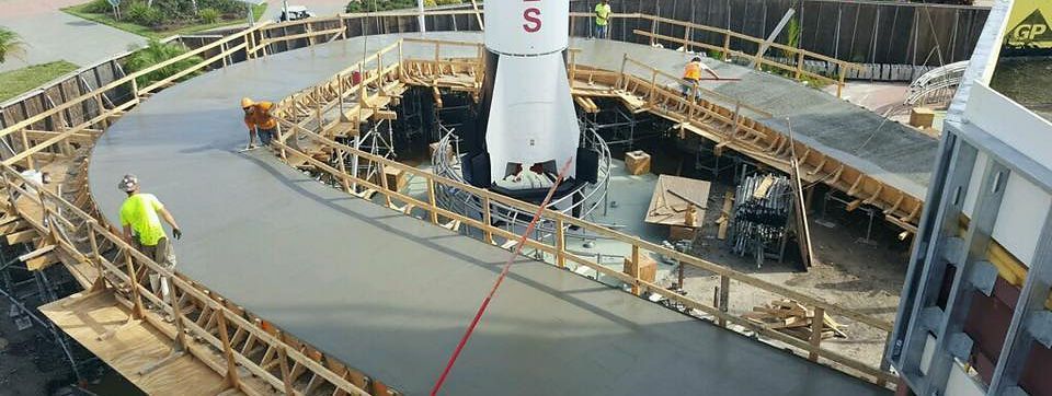 Workers construct a curved concrete platform around the base of a rocket outdoors.