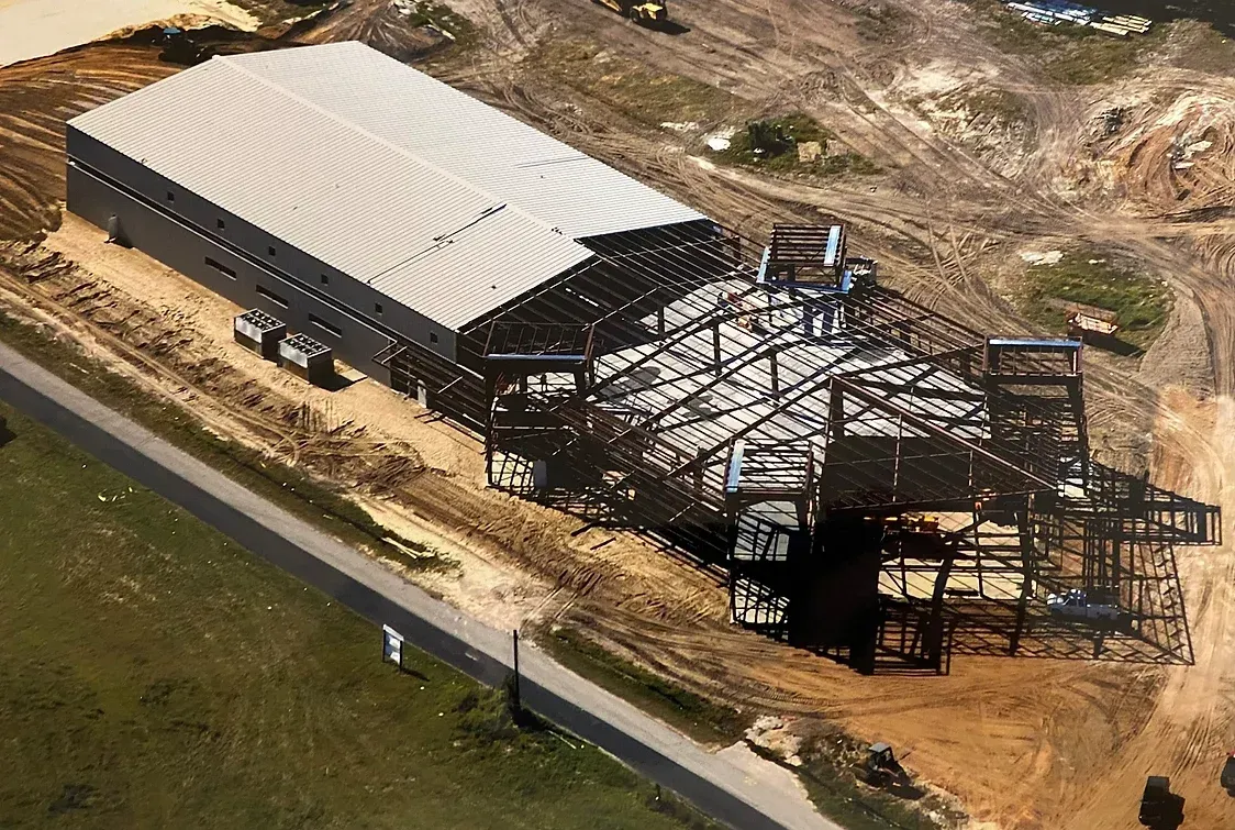 Aerial view of an industrial building under construction, featuring a finished roof section and an exposed steel frame.