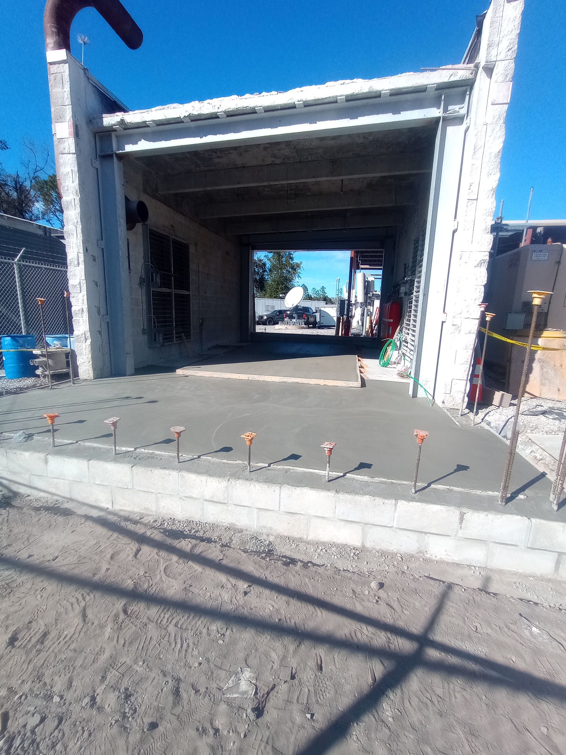 A newly poured concrete entryway leading into a roofed open garage structure under a clear blue sky.