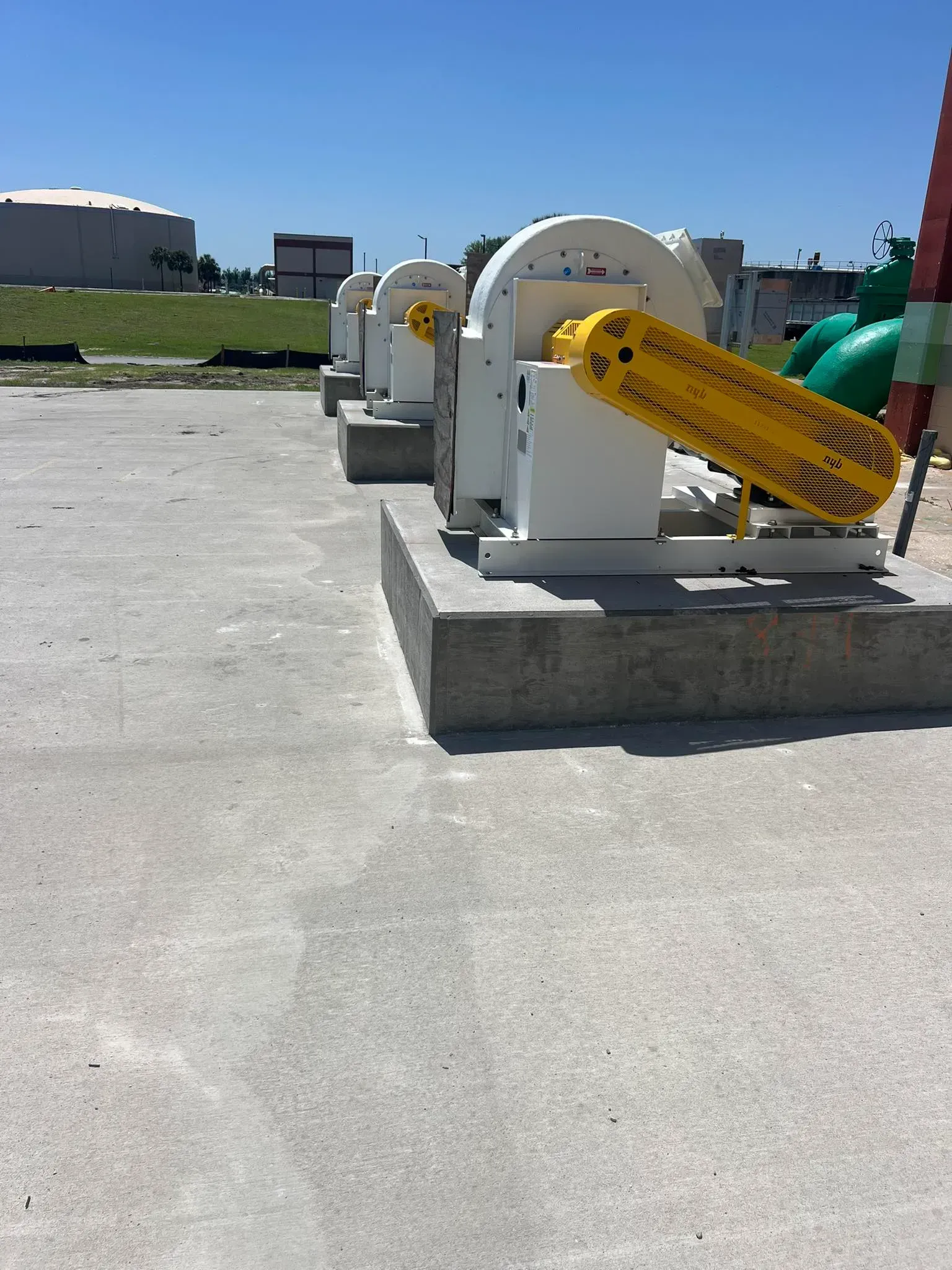 Three industrial blowers with bright yellow safety covers mounted on concrete pads in an outdoor facility.