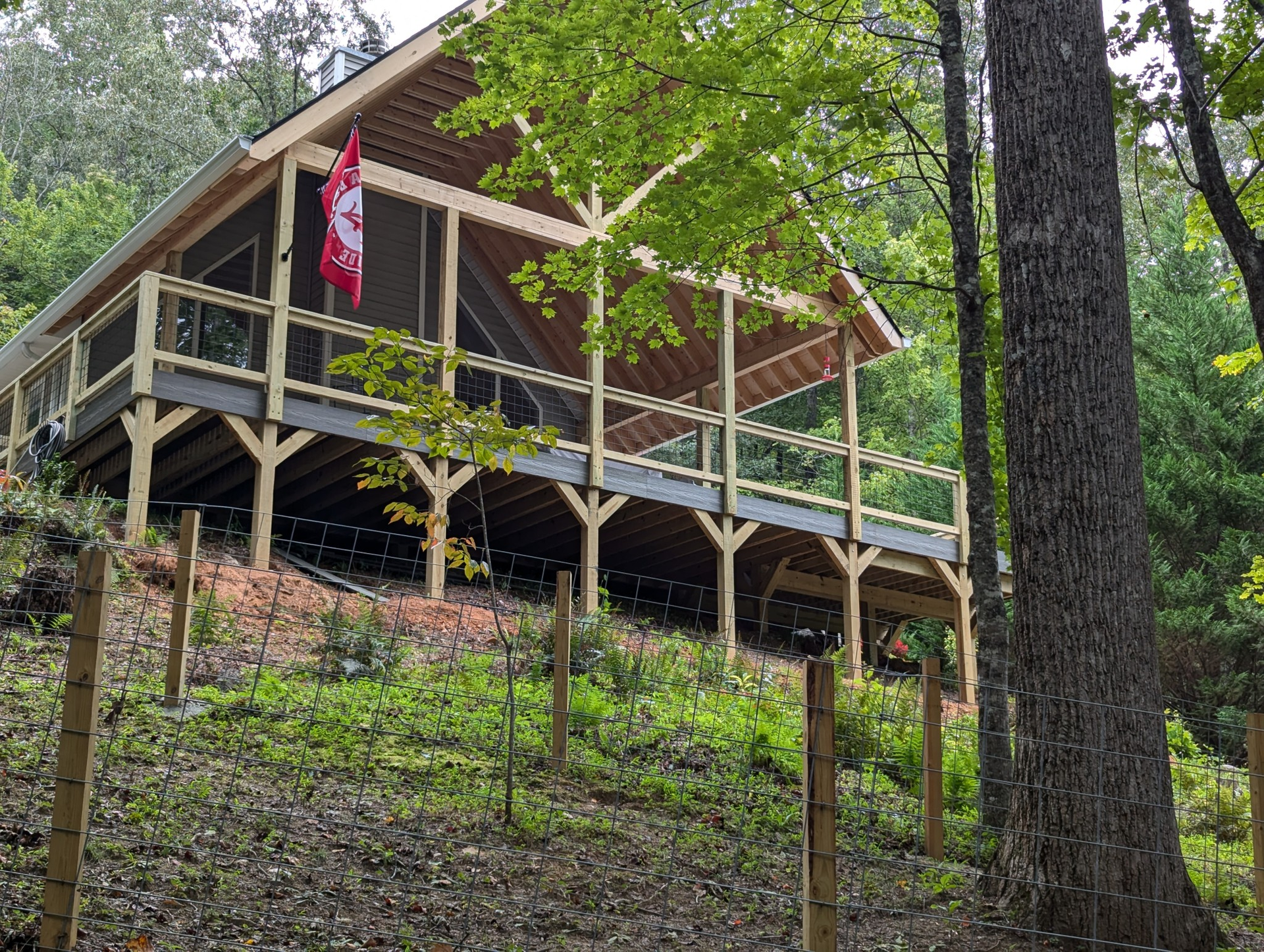 Cabin with wooden deck on a hillside; trees surround it. A flag hangs from the porch.