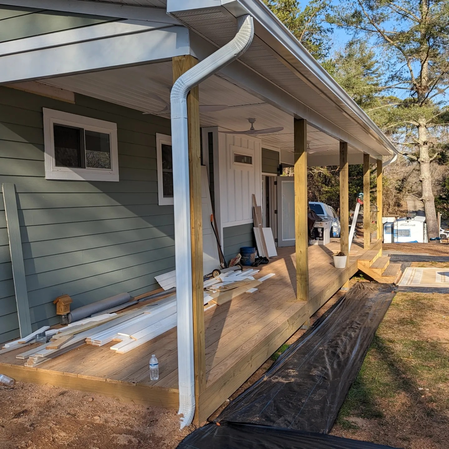 House with porch under construction, green siding, wooden deck, white trim, and a white gutter.
