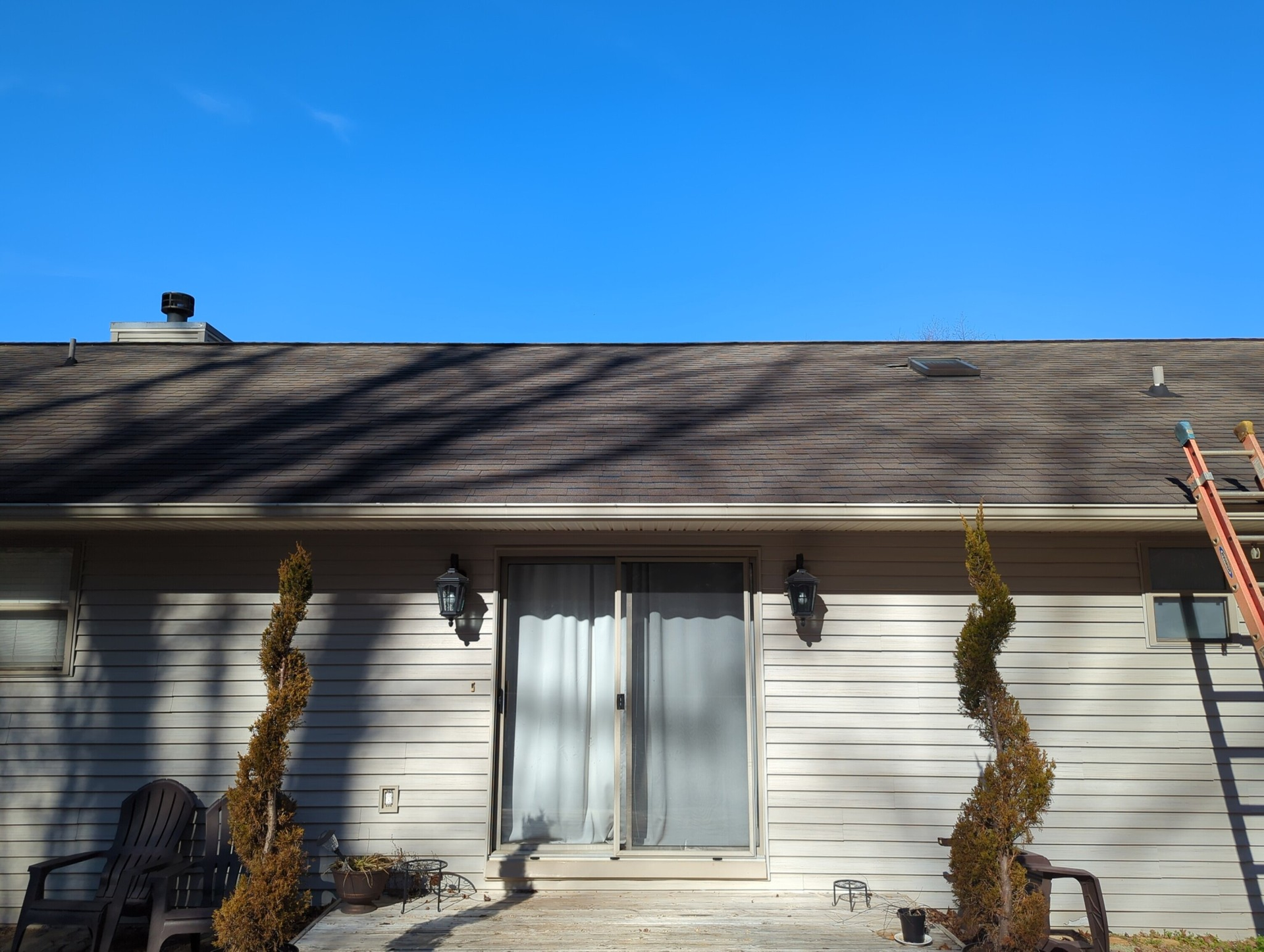 A one-story beige house with a sliding glass door, brown roof, and blue sky.