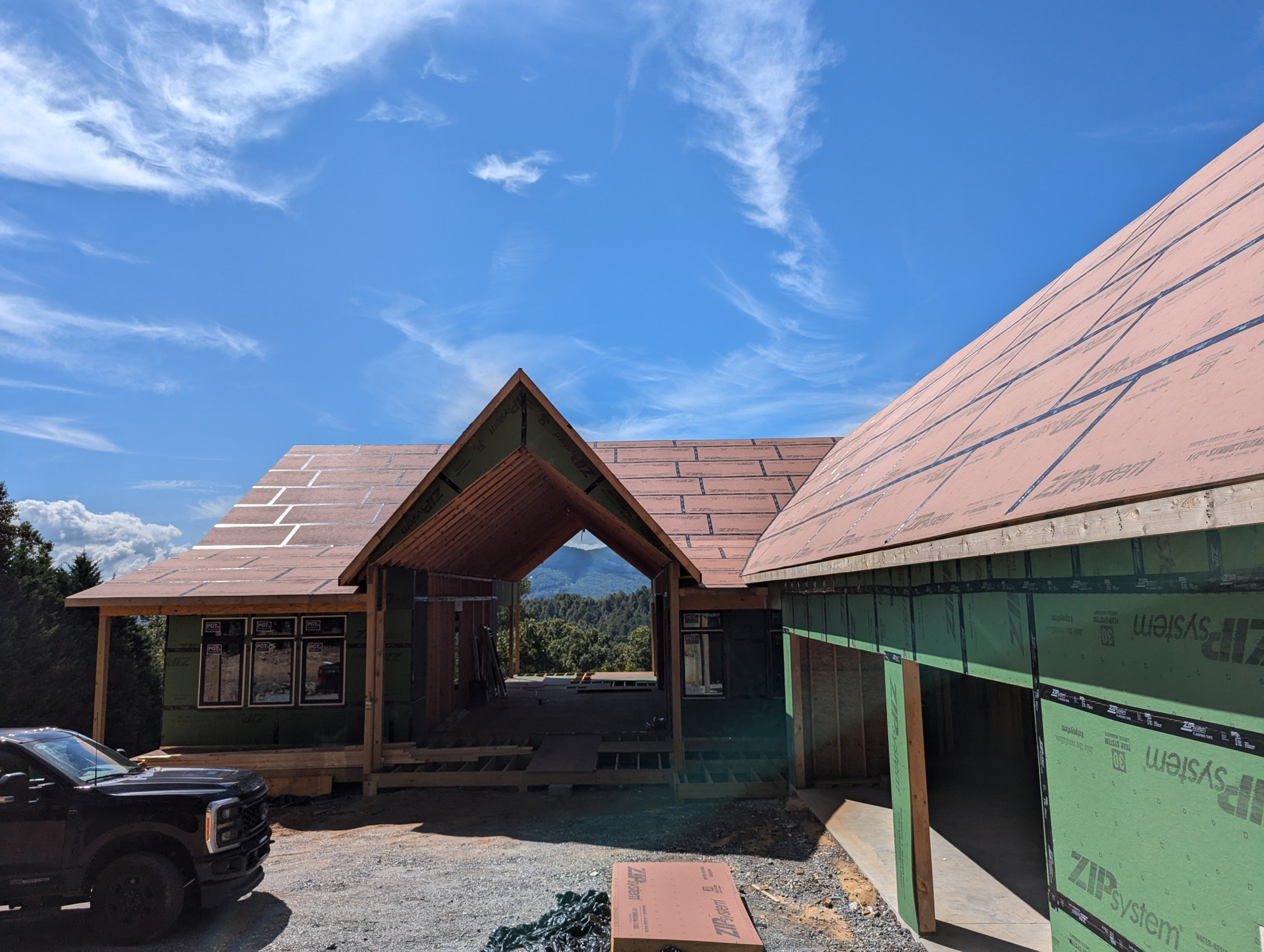 House under construction with blue sky, partially framed with sheathing, and a truck parked in the foreground.
