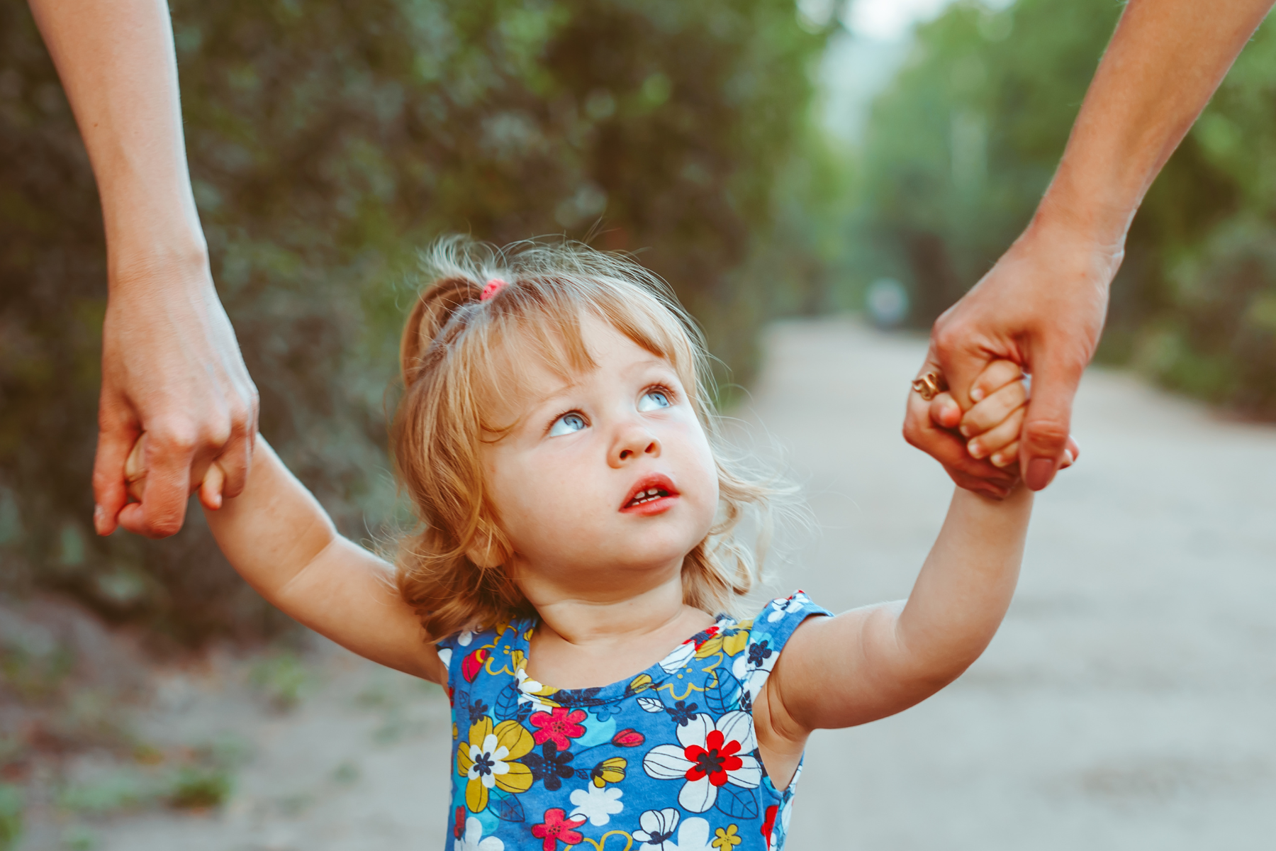 A little girl is holding the hands of her parents.