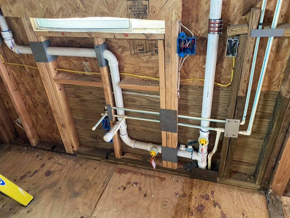 Exposed plumbing and electrical wiring inside a wall frame during home construction.