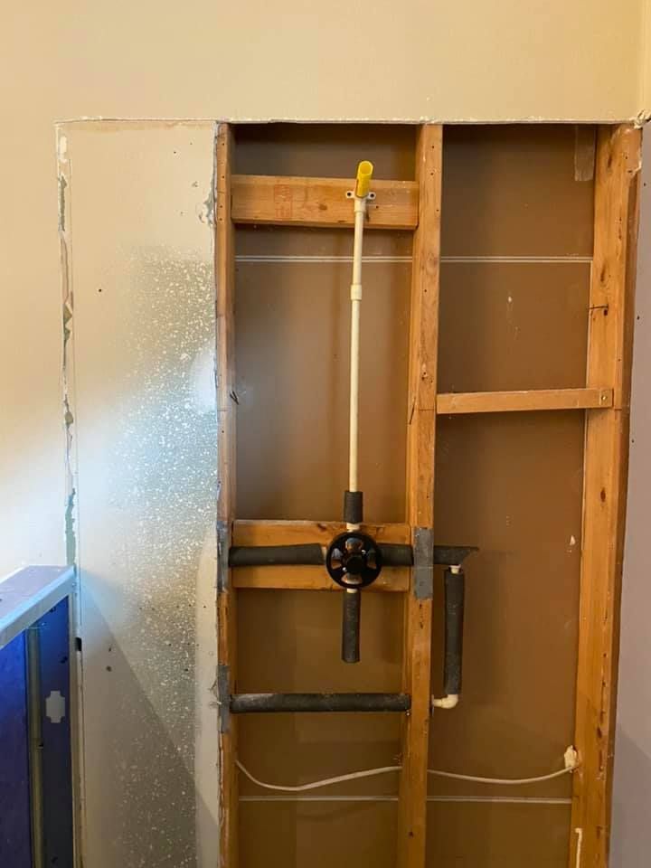 Partially tiled wall with exposed studs and a shower valve, under renovation